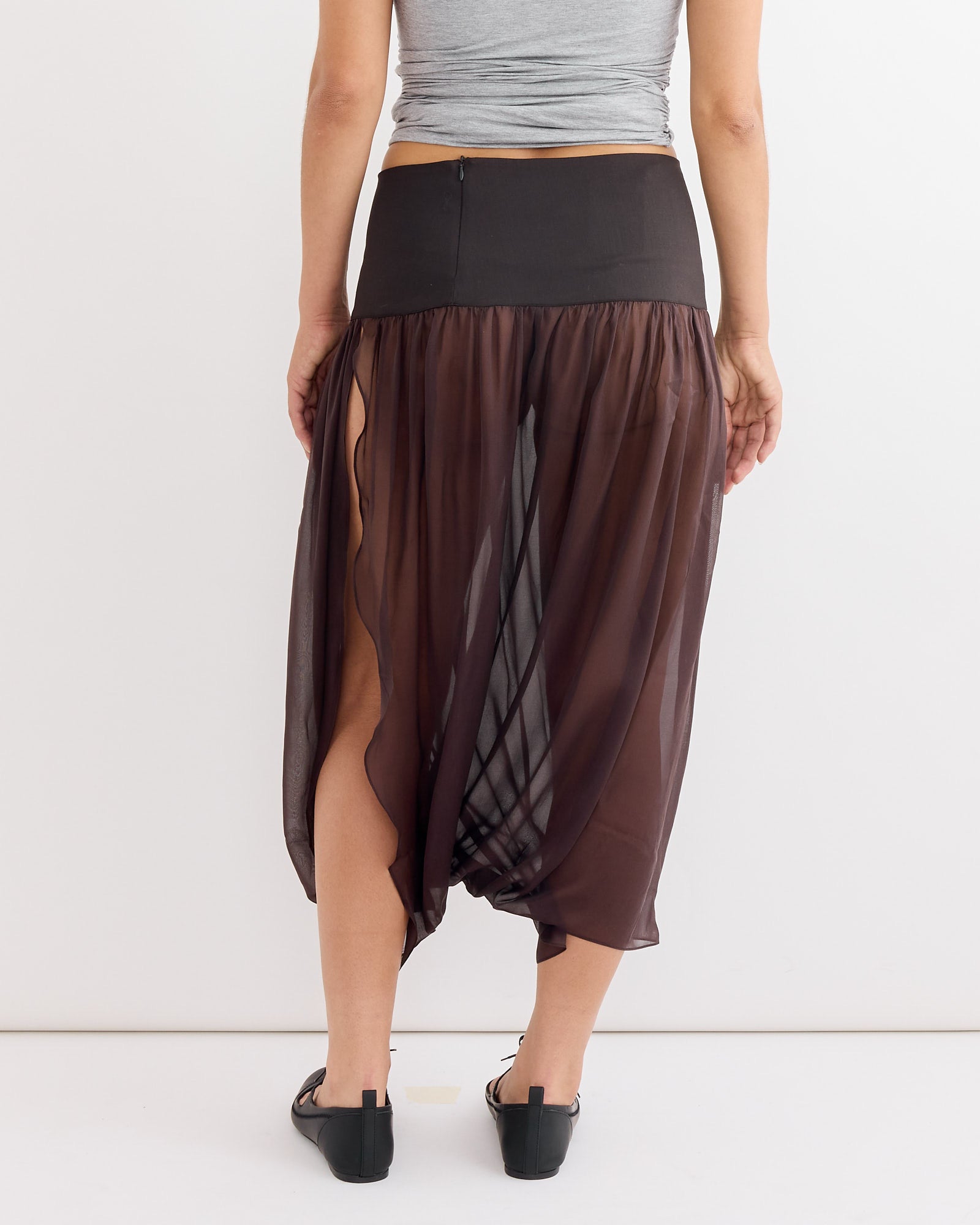 A person wearing the Paloma Wool Mila Skirt in Brown, which features a sheer silk fabric and a tailored waistband.