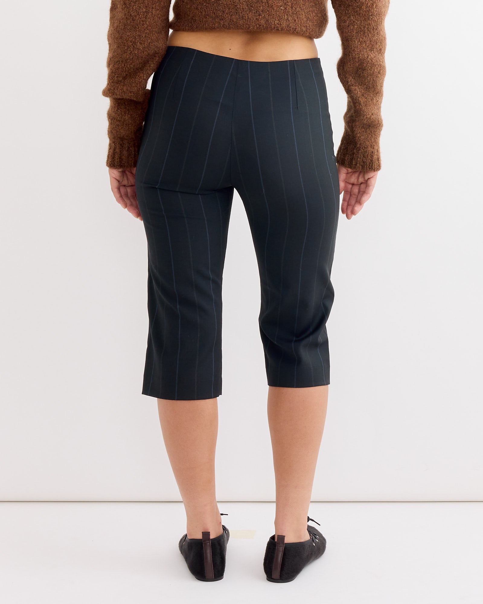 A person stands facing away, wearing Paloma Wool Tinas Pant in Blue, a brown long-sleeve top, and black flats against a plain white background.