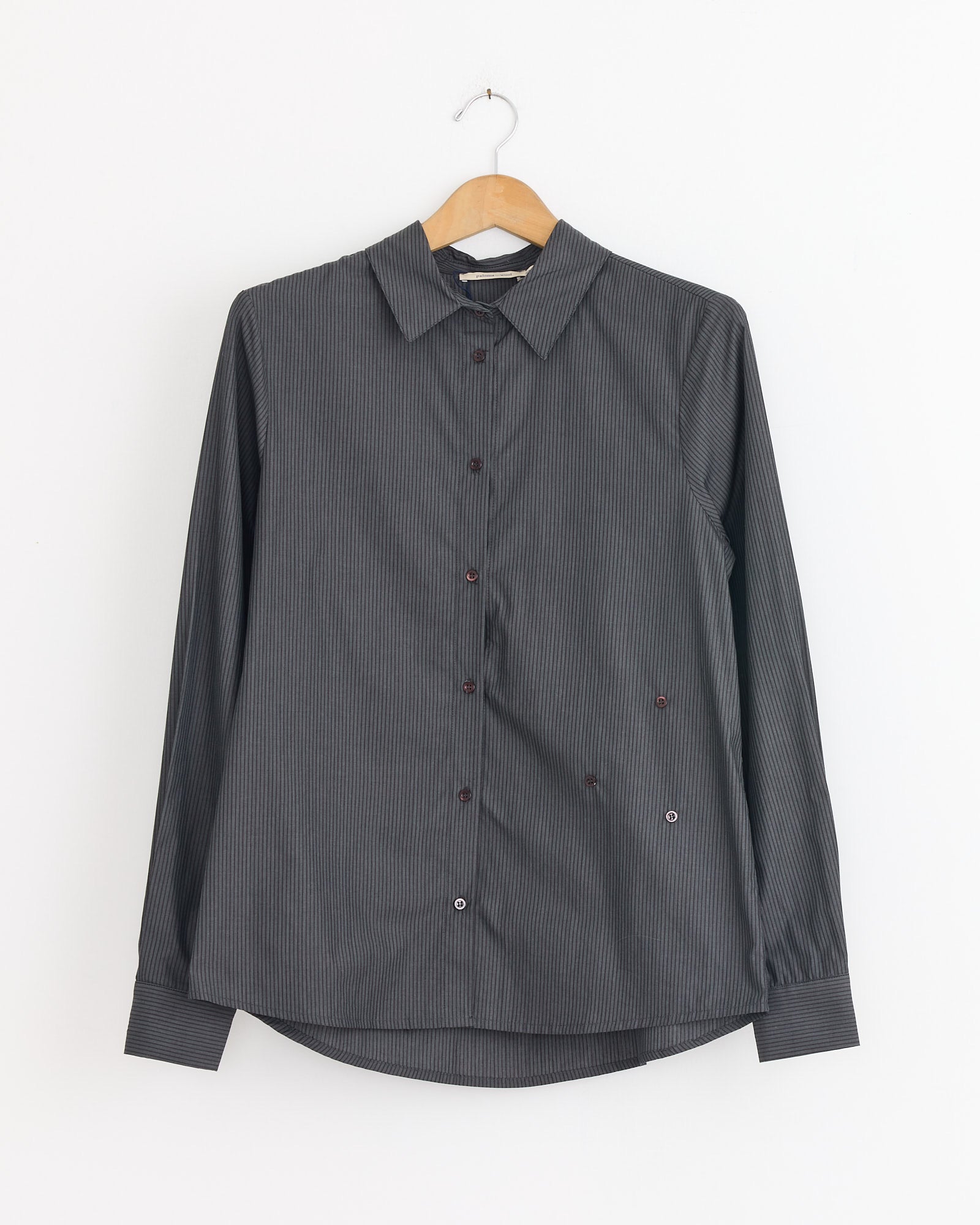 A Paloma Wool Donald Shirt in Black with long sleeves and a subtle pinstripe pattern hangs on a wooden hanger against a plain white wall.