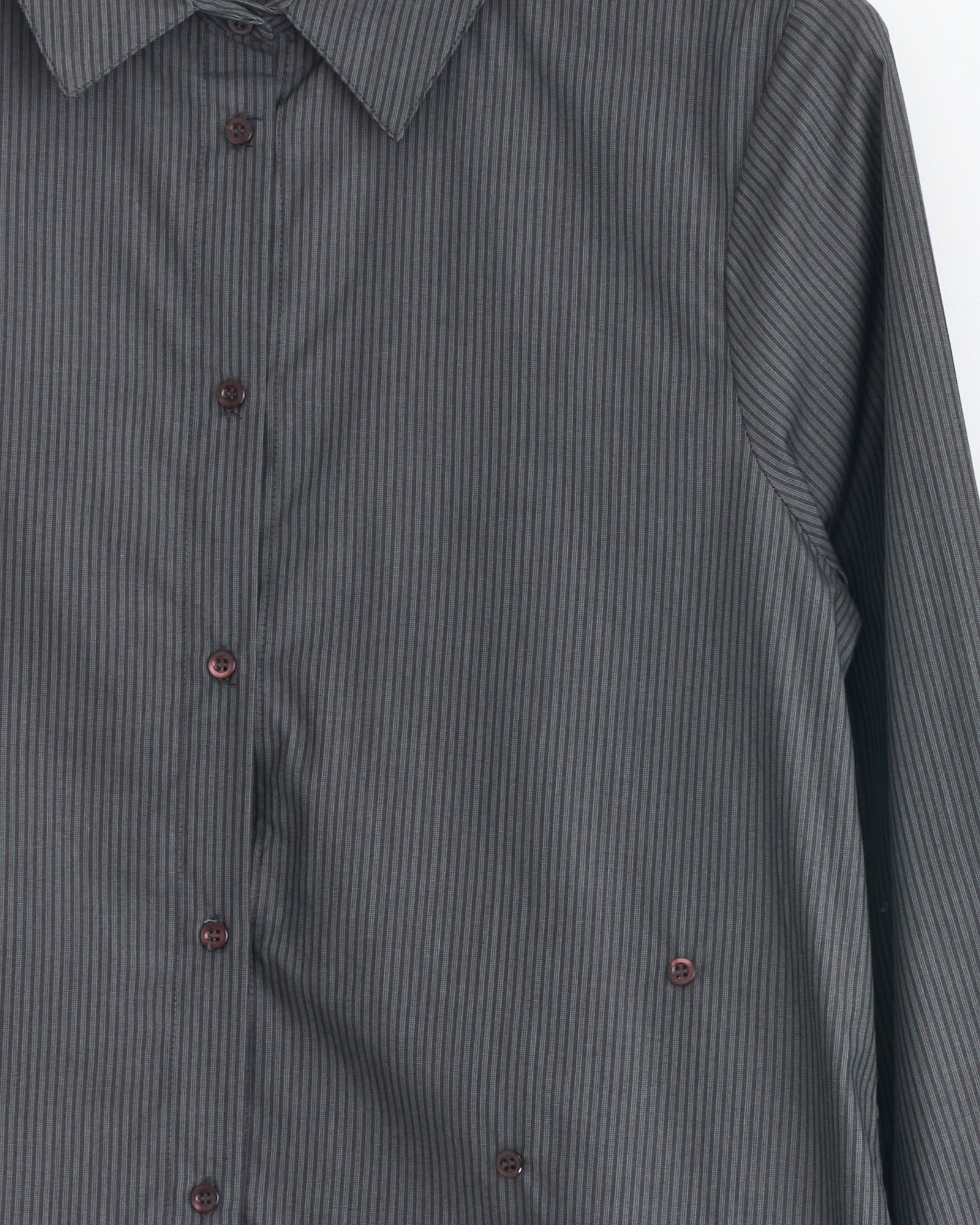 A close-up of the Paloma Wool Donald Shirt in Black, a long-sleeved button-up with thin vertical stripes and brown buttons. Part of the front, collar, and one sleeve are visible against a white background.