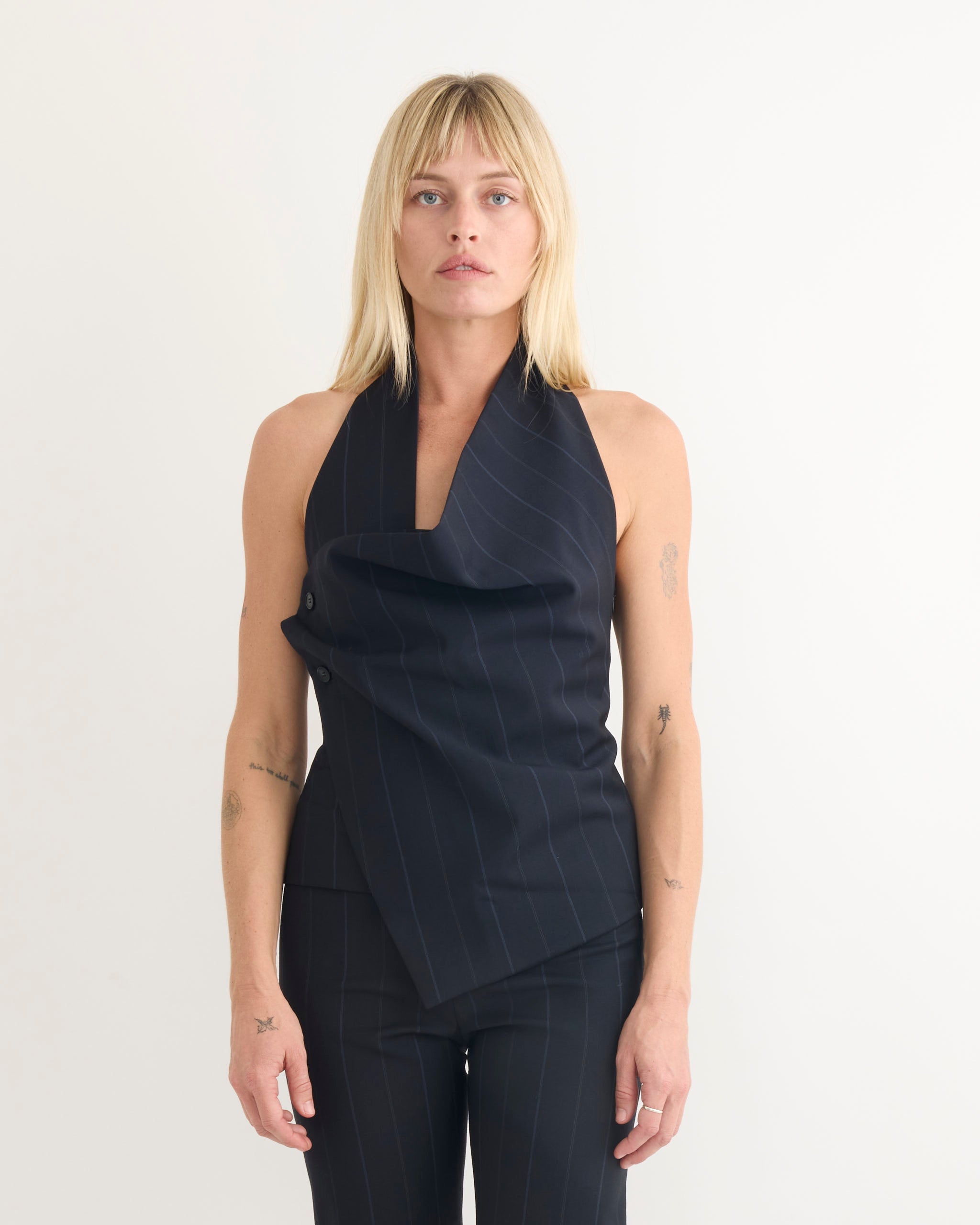 A person with straight blonde hair stands against a plain background, wearing the Paloma Wool Tiomi Top in Blue and matching pants. Their arms are relaxed at their sides as they look directly at the camera.
