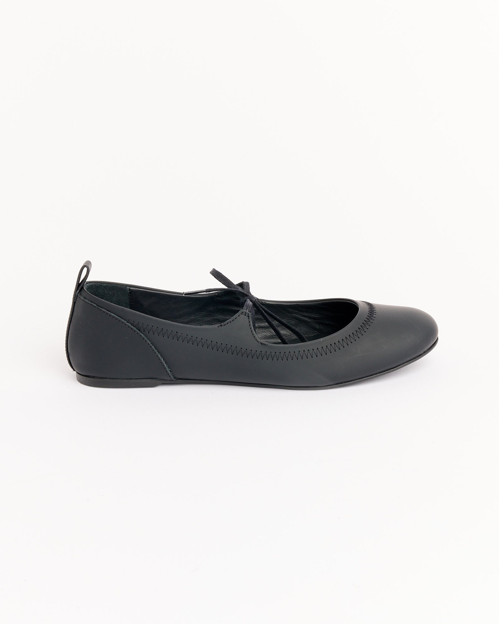 The Zora Rubber Ballet in Black by Paloma Wool features a rounded toe, crisscross upper straps, and a small heel pull tab, shown against a plain white background.