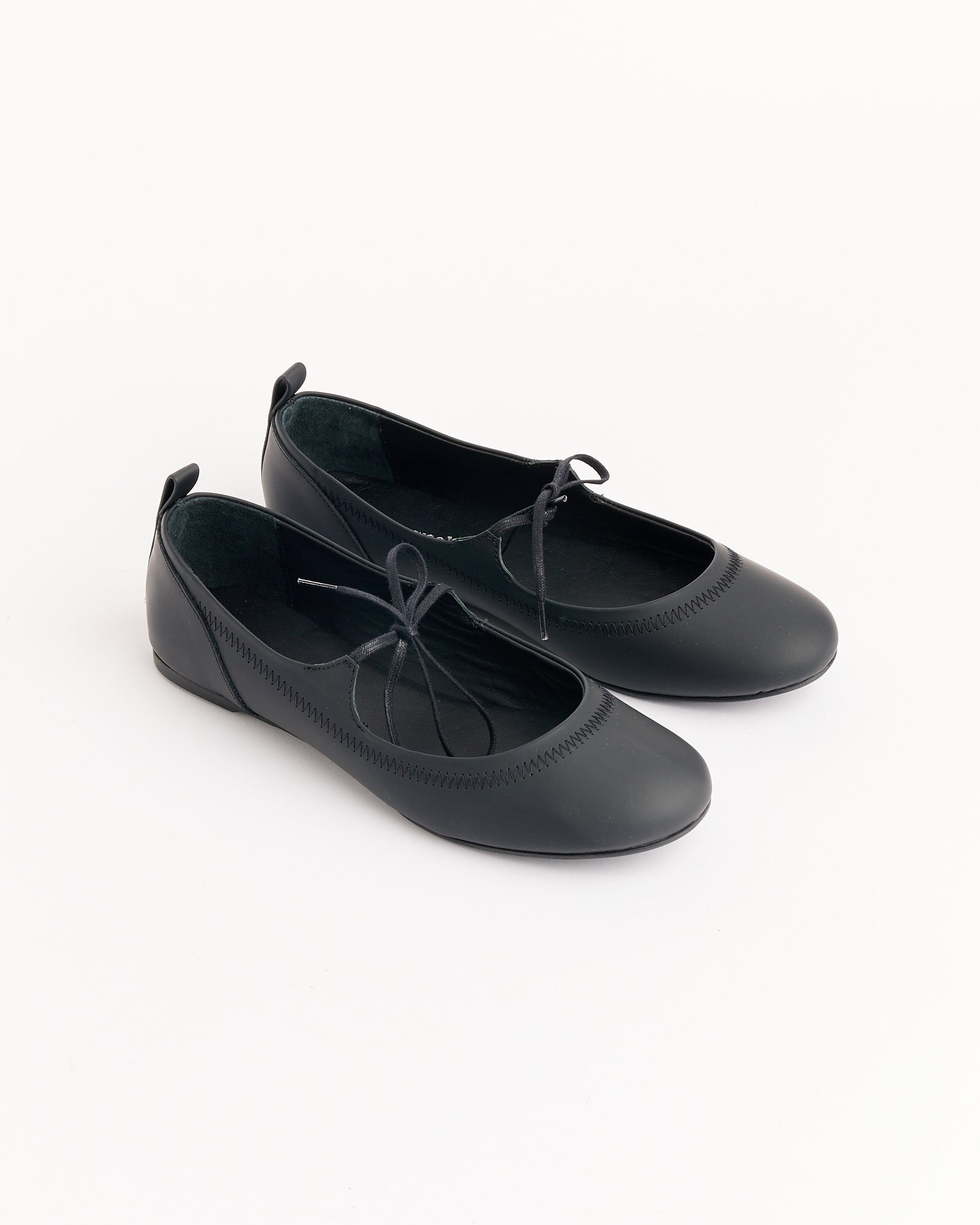 A pair of Paloma Wool Zora Rubber Ballet flats in black, featuring rounded toes, thin bow-tied laces, and low heels, displayed on a white background.