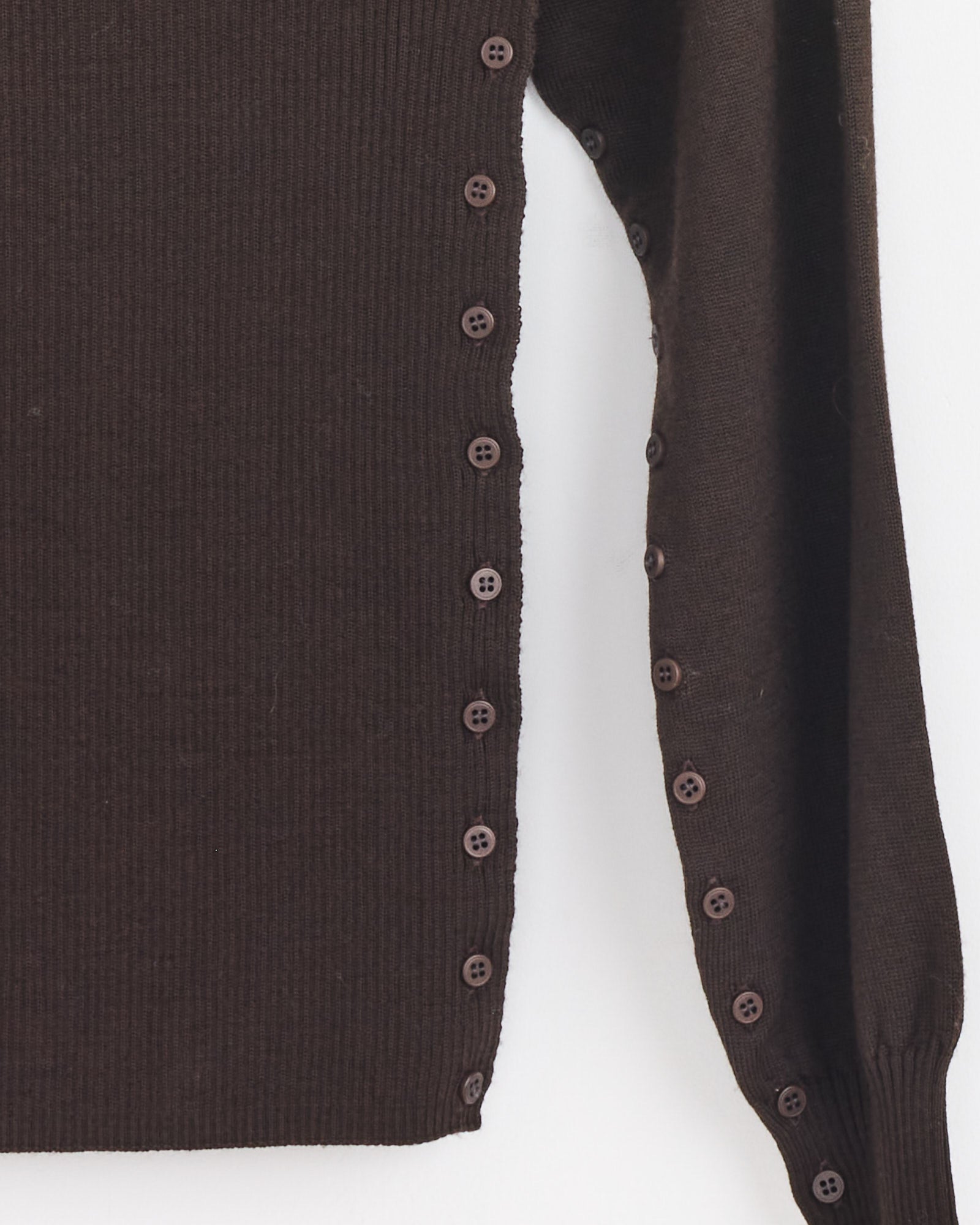 Close-up of the Paloma Wool Fa Sweater in Brown showing its right sleeve and side, with matching brown buttons along the side seam and sleeve cuff. Made from extrafine merino wool in Spain.