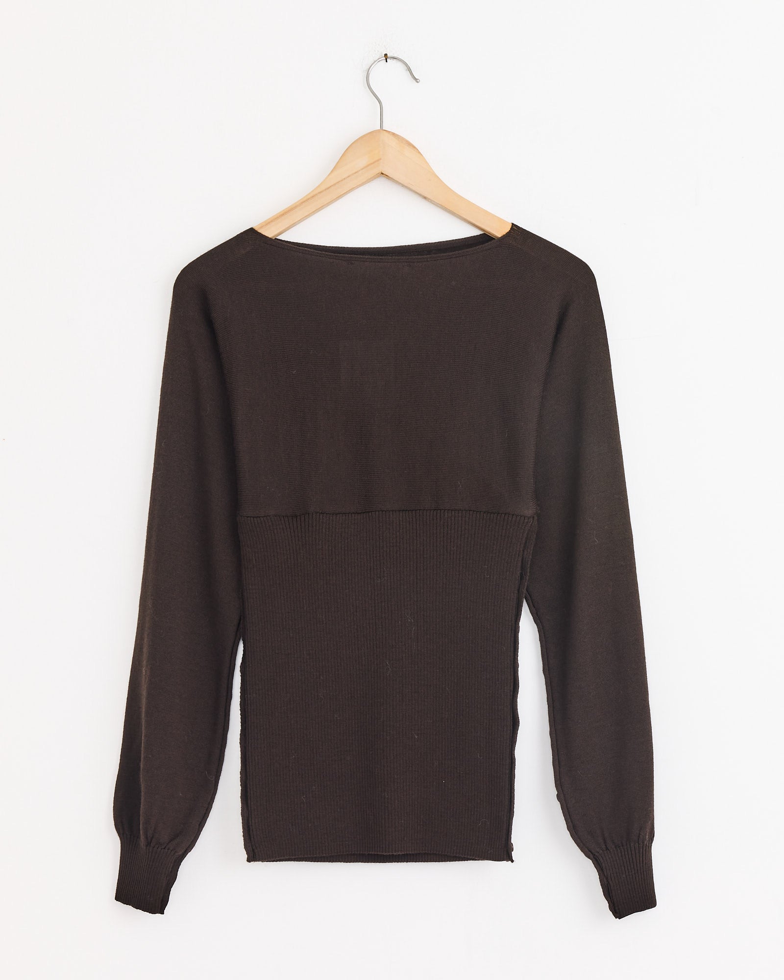 The Paloma Wool Fa Sweater in Brown, made from extrafine merino wool, hangs on a wooden hanger against a white background and features long sleeves, a wide neckline, ribbed cuffs, and a ribbed waistband.