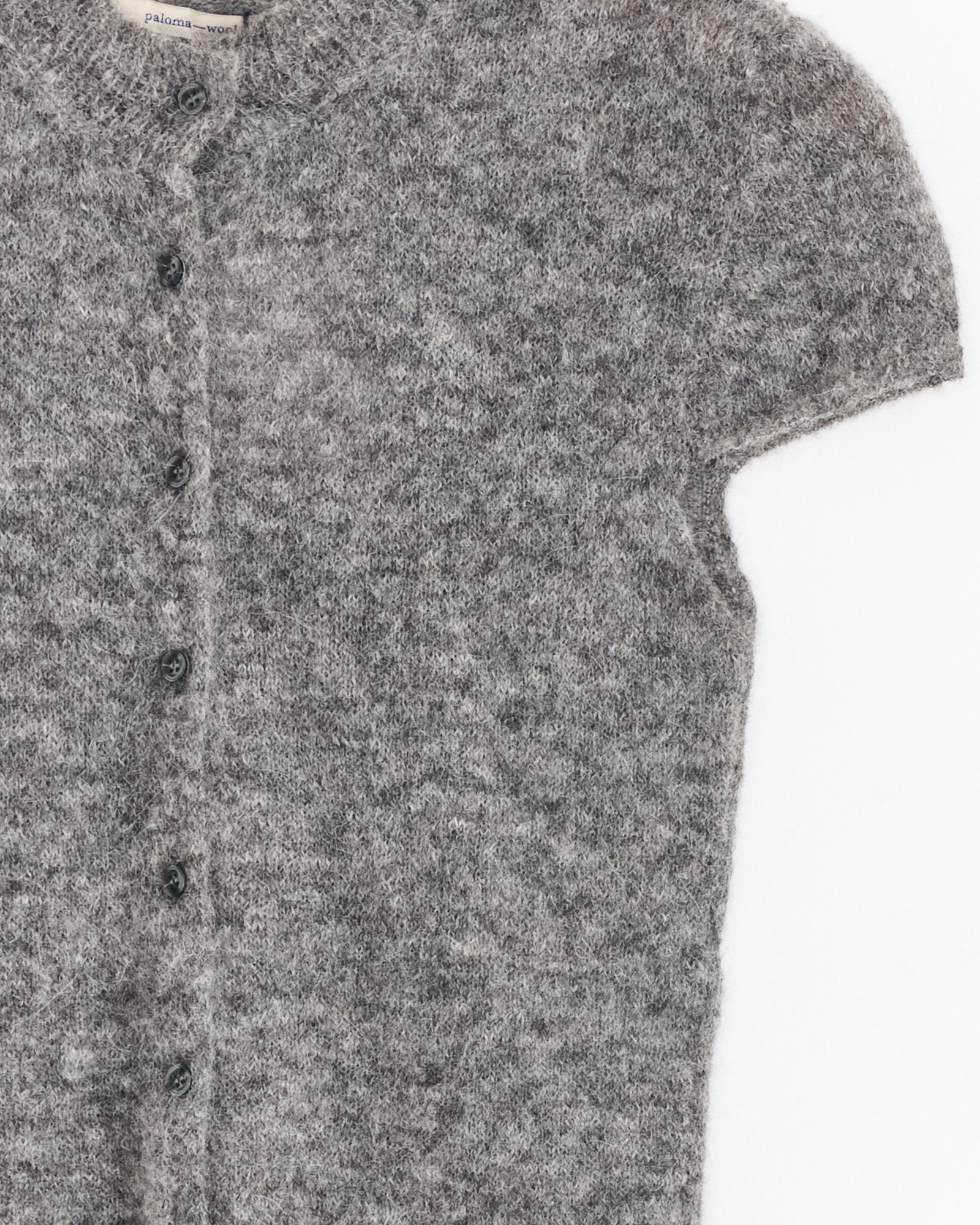 A close-up of the Paloma Wool Refian Sweater in Grey, a fuzzy, fitted short-sleeve cardigan with front buttons, made from Responsible Finealpaca, displayed on a flat white background.