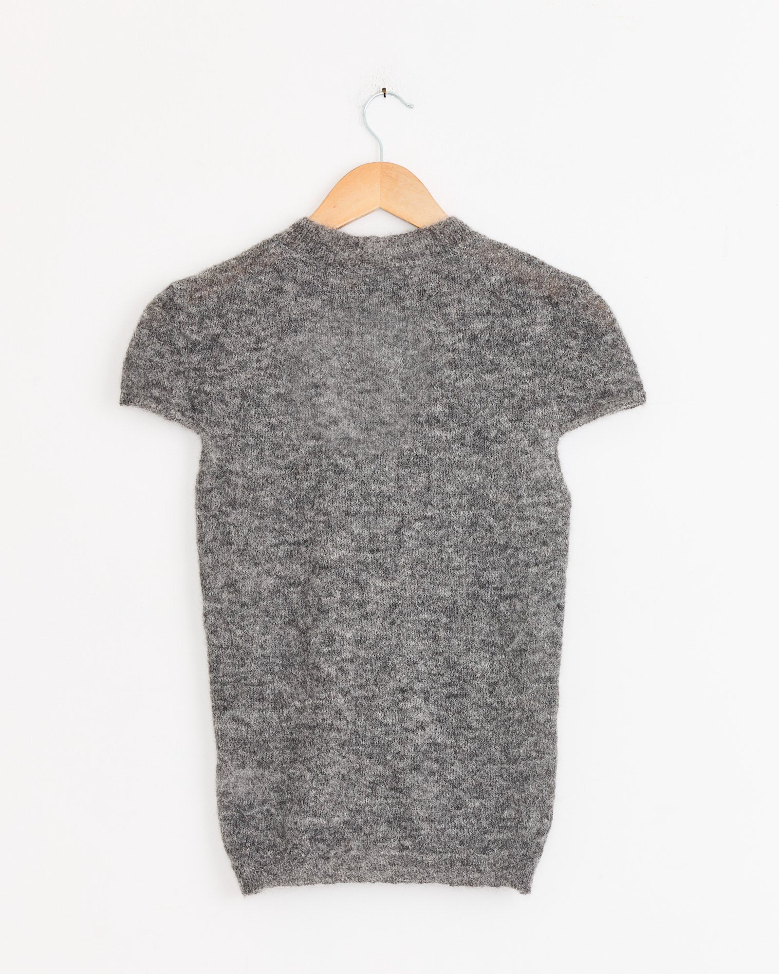 The Paloma Wool Refian Sweater in Grey, a fuzzy knit fitted short-sleeve cardigan, is displayed from the back on a wooden hanger against a plain white background.