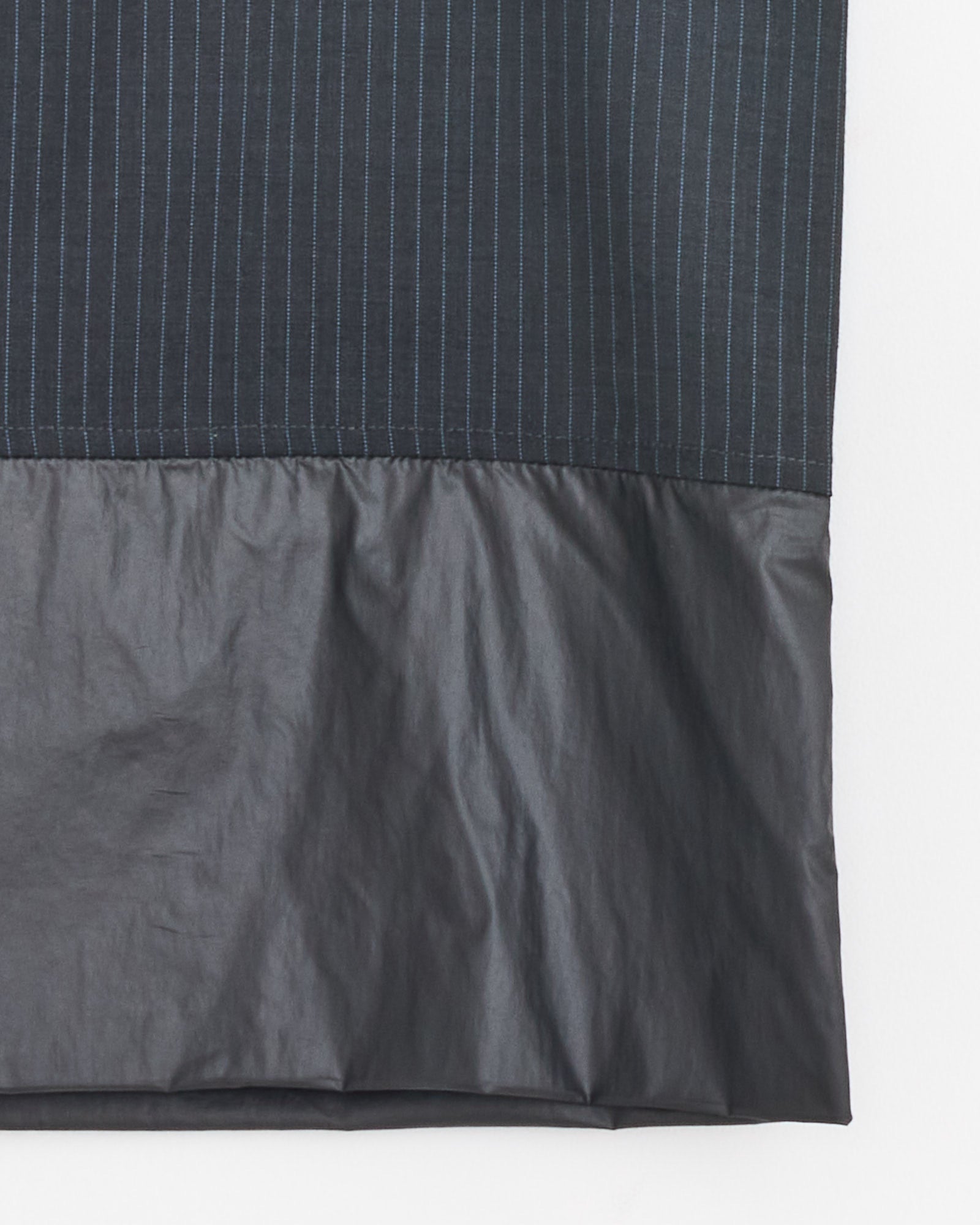 A close-up of Paloma Wool's Ongi Skirt in Grey shows two textures: the upper part features dark grey pinstripes, while the lower section is smooth and solid—perfect for a structured, knee-length look.