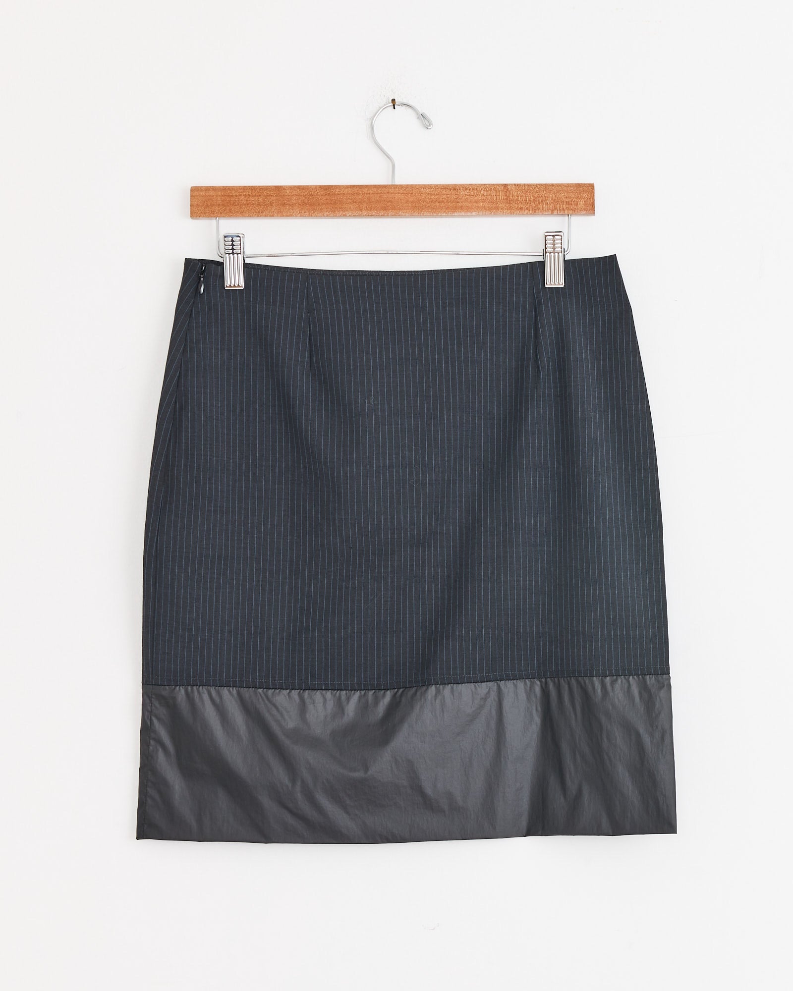 The Ongi Skirt in Grey by Paloma Wool is a structured, knee-length piece made from dark gray suiting fabric with a solid hem, shown on a wooden hanger against a white background.