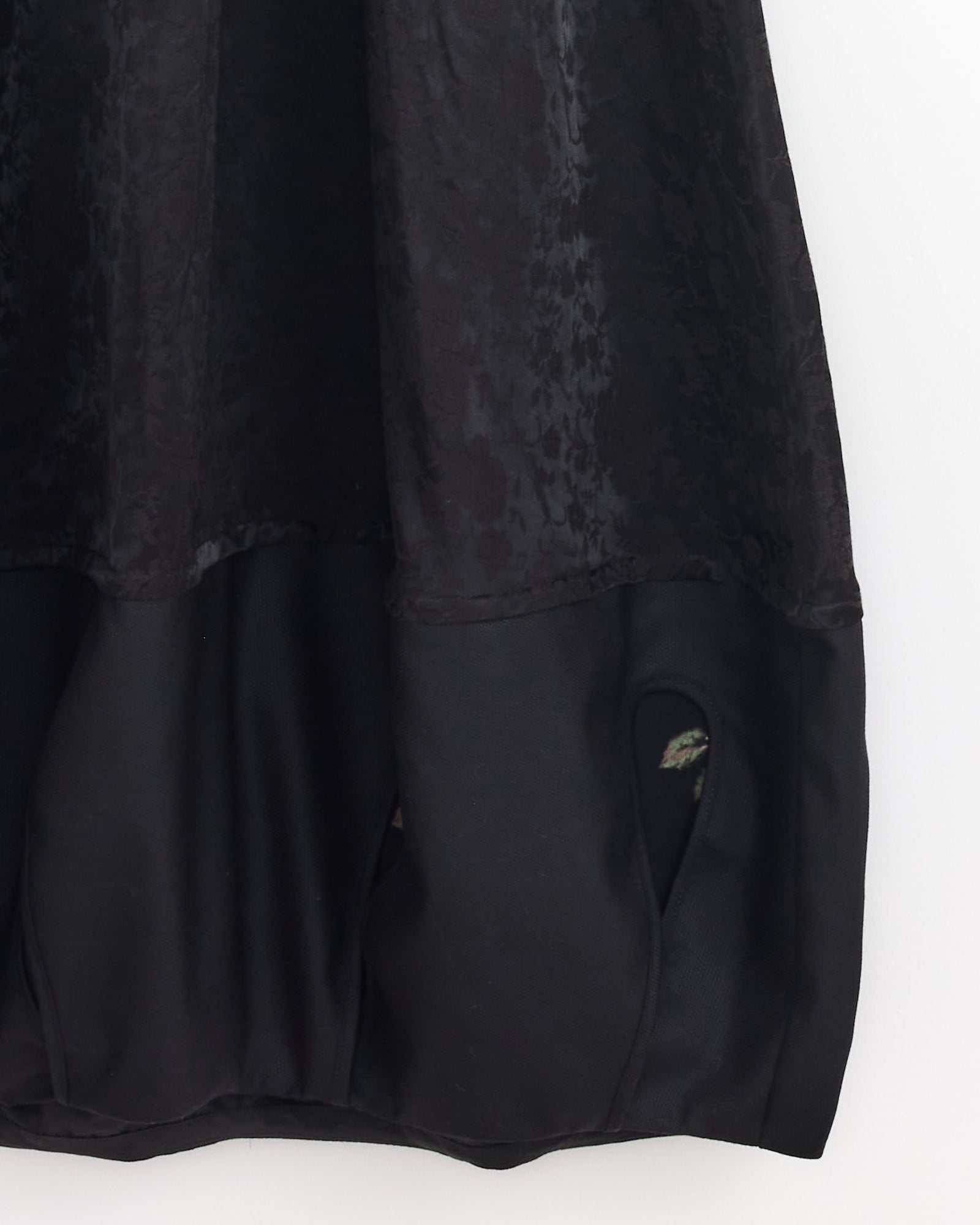A close-up of the Rattle Dress in Black by J. Kim, showing a textured jacquard viscose lower portion with a smooth hem band and small oval cutouts near the edge.