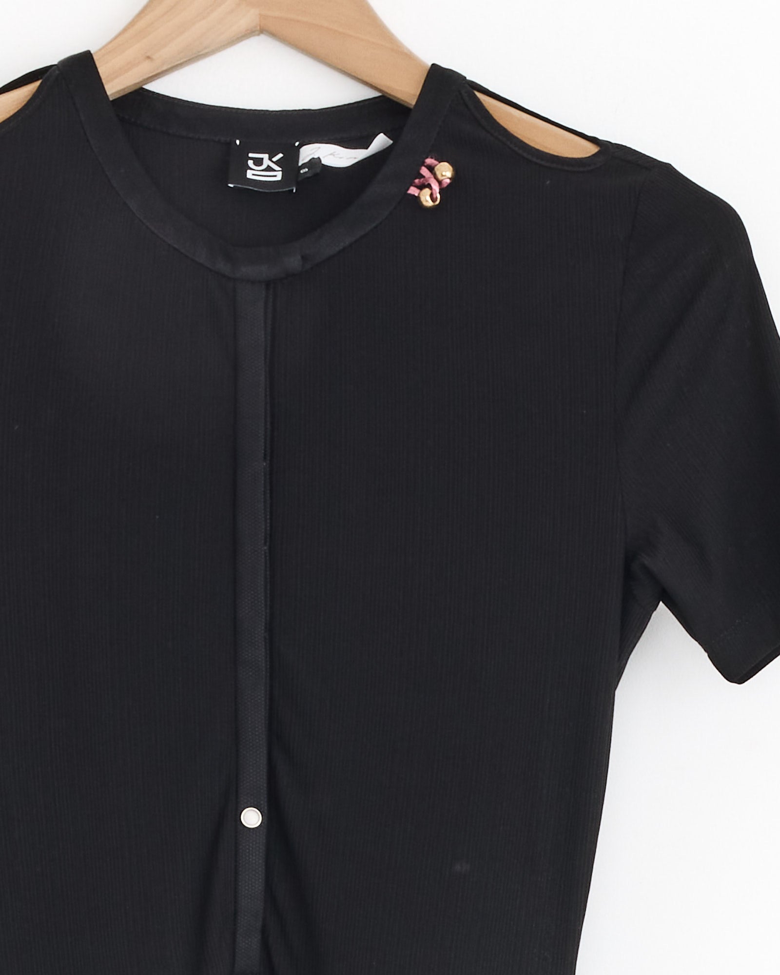 The Rattle Dress in Black by J. Kim is a short-sleeved silk dress with a round neckline, displayed on a hanger, and adorned with a small purple and gold brooch on the right shoulder.