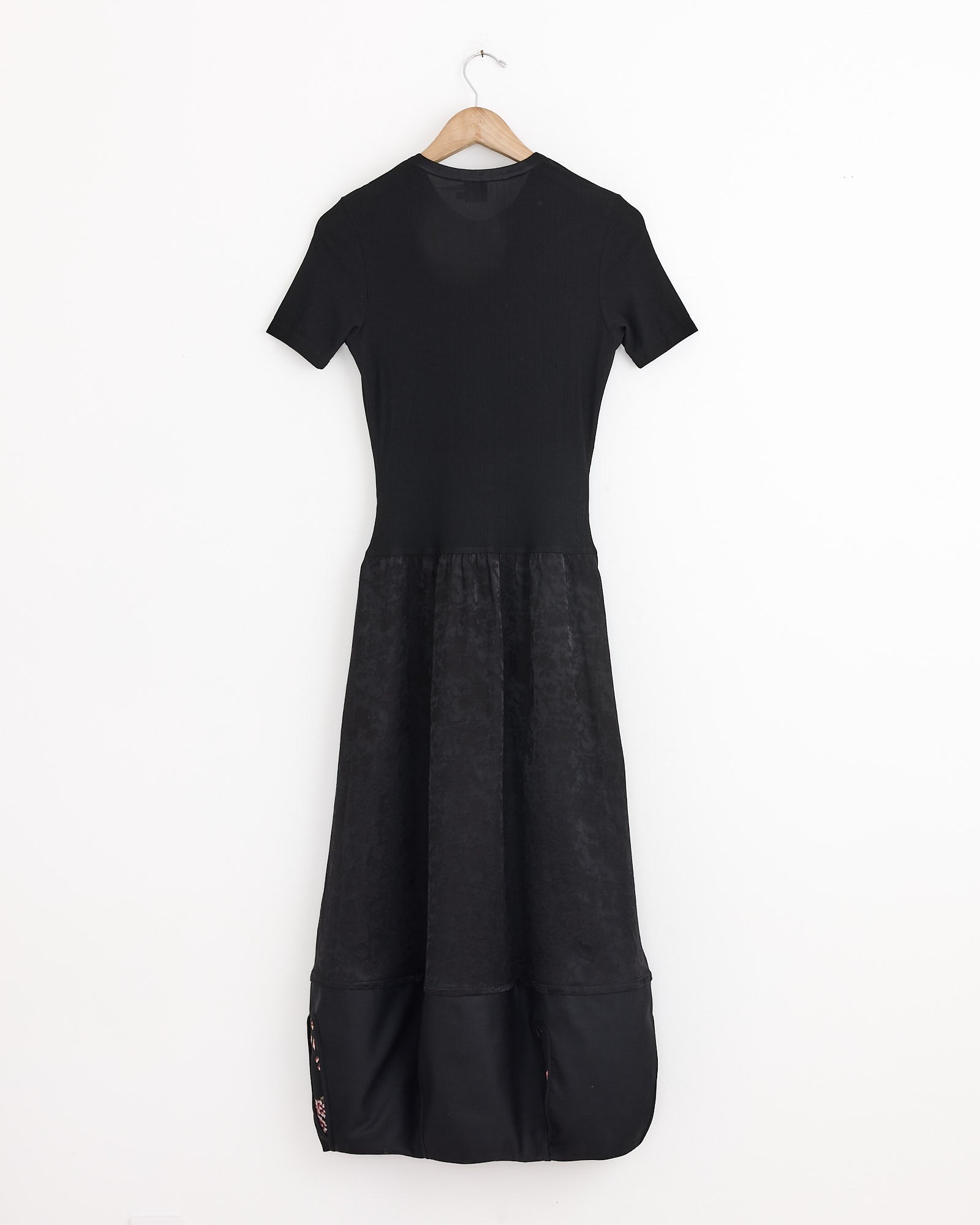 The J. Kim Rattle Dress in Black features a fitted silk top, flared jacquard viscose skirt, and subtle floral patterns near the hem, displayed on a wooden hanger against a plain white background.