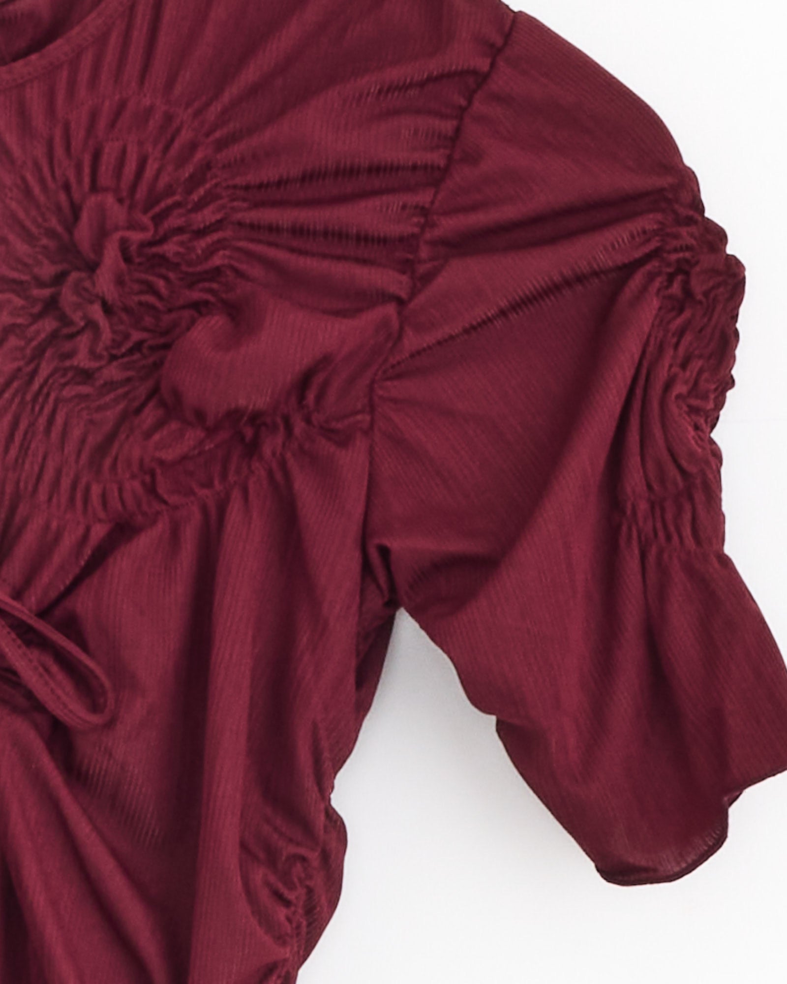 A close-up of the J. Kim Markiza Dress in Burgundy, showcasing short sleeves and gathered, ruched detailing around the shoulders and chest, set against a plain white background.