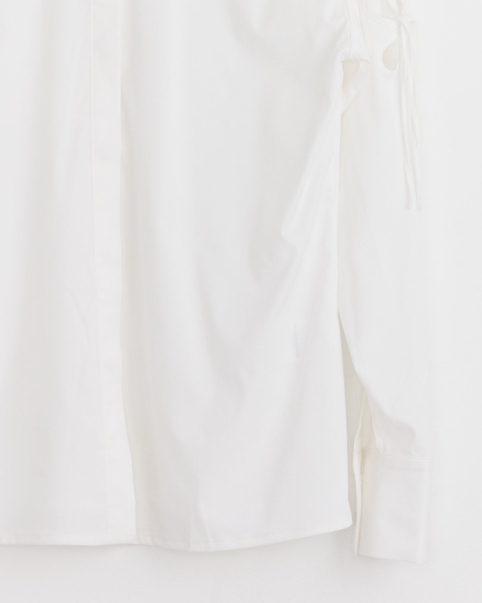 The J. Kim Petal Shirt in White is a long-sleeve, loose-fit cotton poplin shirt with visible cuffs and a tied upper sleeve detail, displayed against a white background.