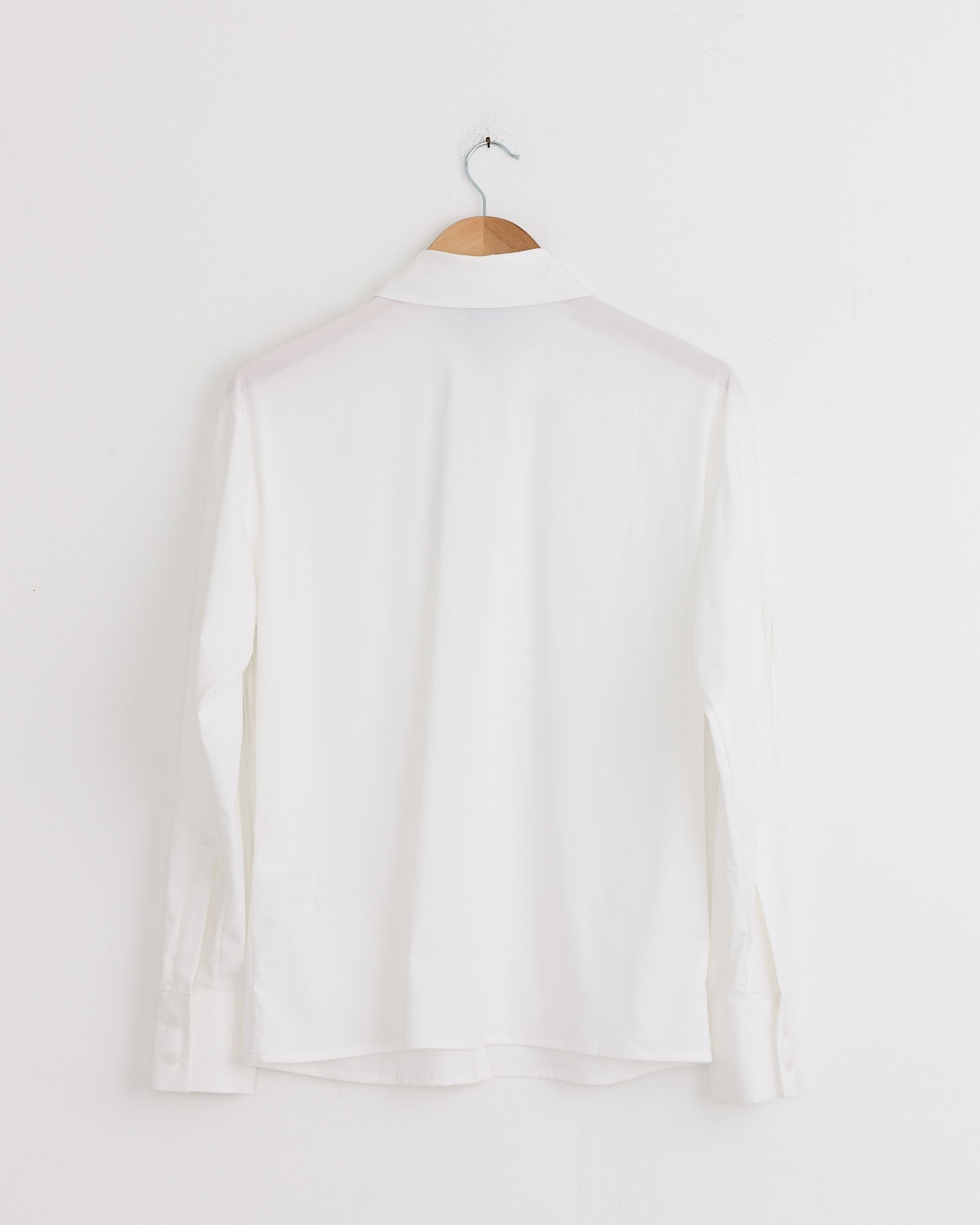 The Petal Shirt in White by J. Kim is displayed from the back, hanging on a wooden hanger against a white wall.