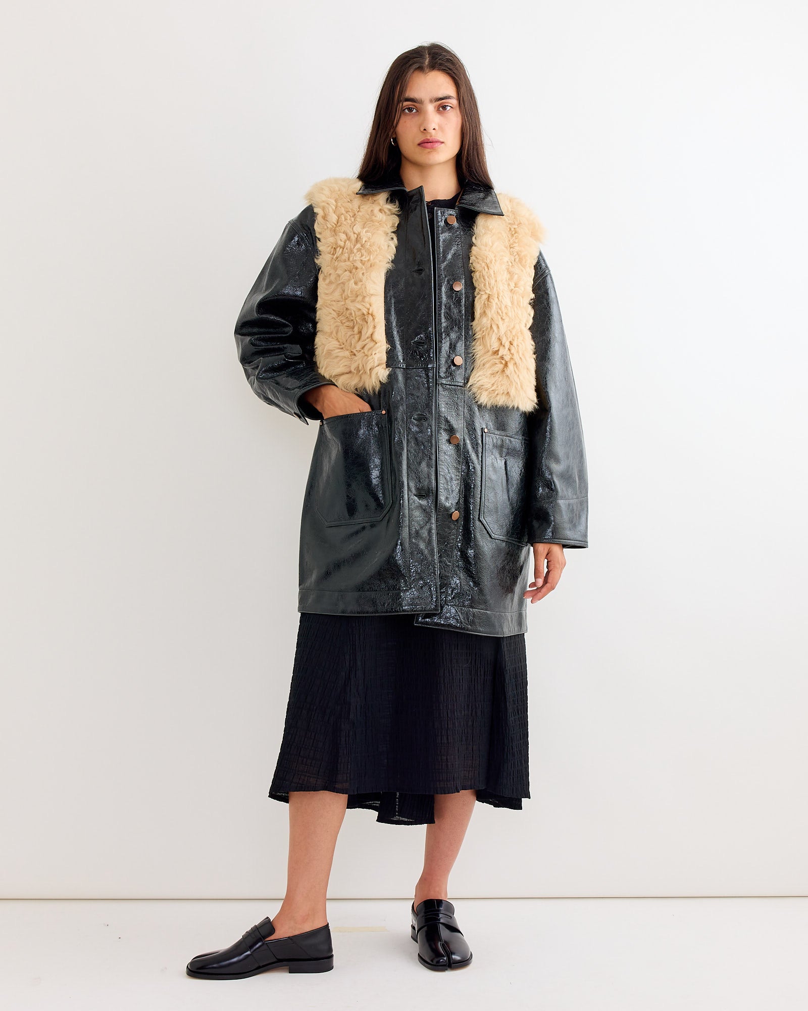 A woman in the Milena Silvano Chore Coat in Black Mix stands confidently, its black suede adding a luxurious touch to her timeless style.