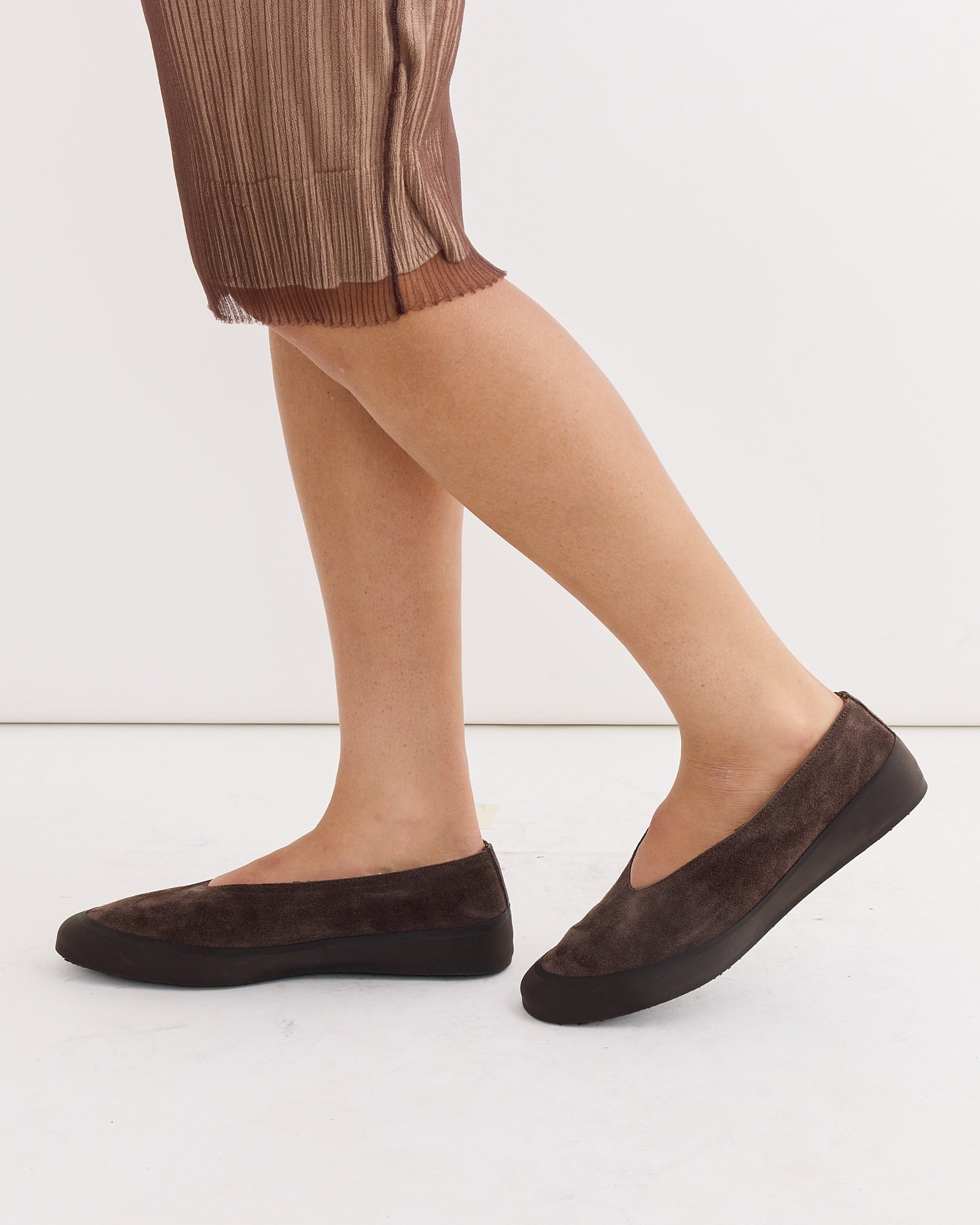 A person stands against a white background wearing a brown pleated skirt and Le Monde Beryl Apres Ski Shoes in Brown, crafted in Italy with dark brown suede uppers and black soles.