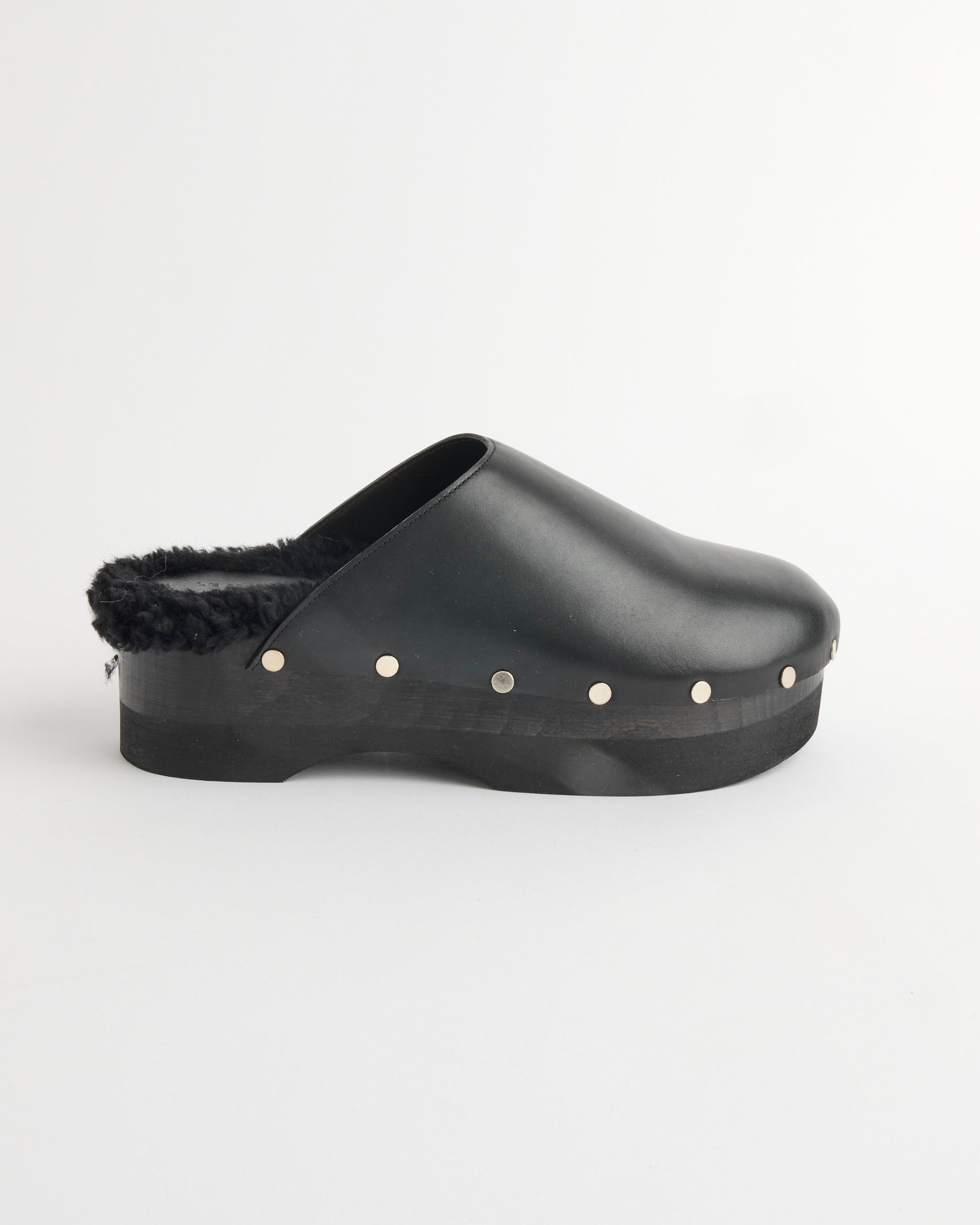 The Le Monde Beryl Clog in Black features a platform sole, faux fur lining, and metallic stud detailing along the edge, shown against a plain white background.