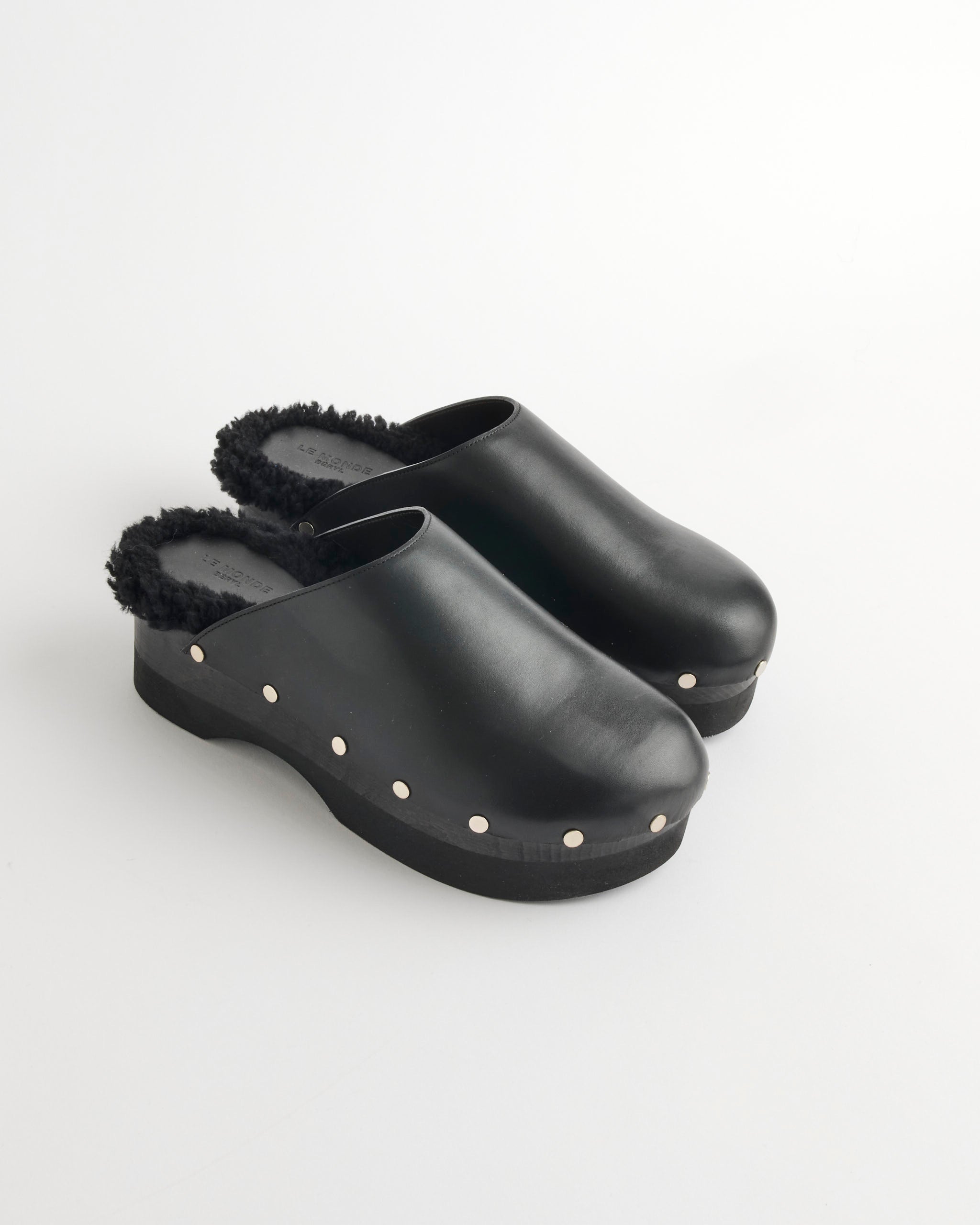Le Monde Beryl's Clog in Black features black leather, faux fur lining, silver side studs, and a cozy shearling insole, shown against a white background.