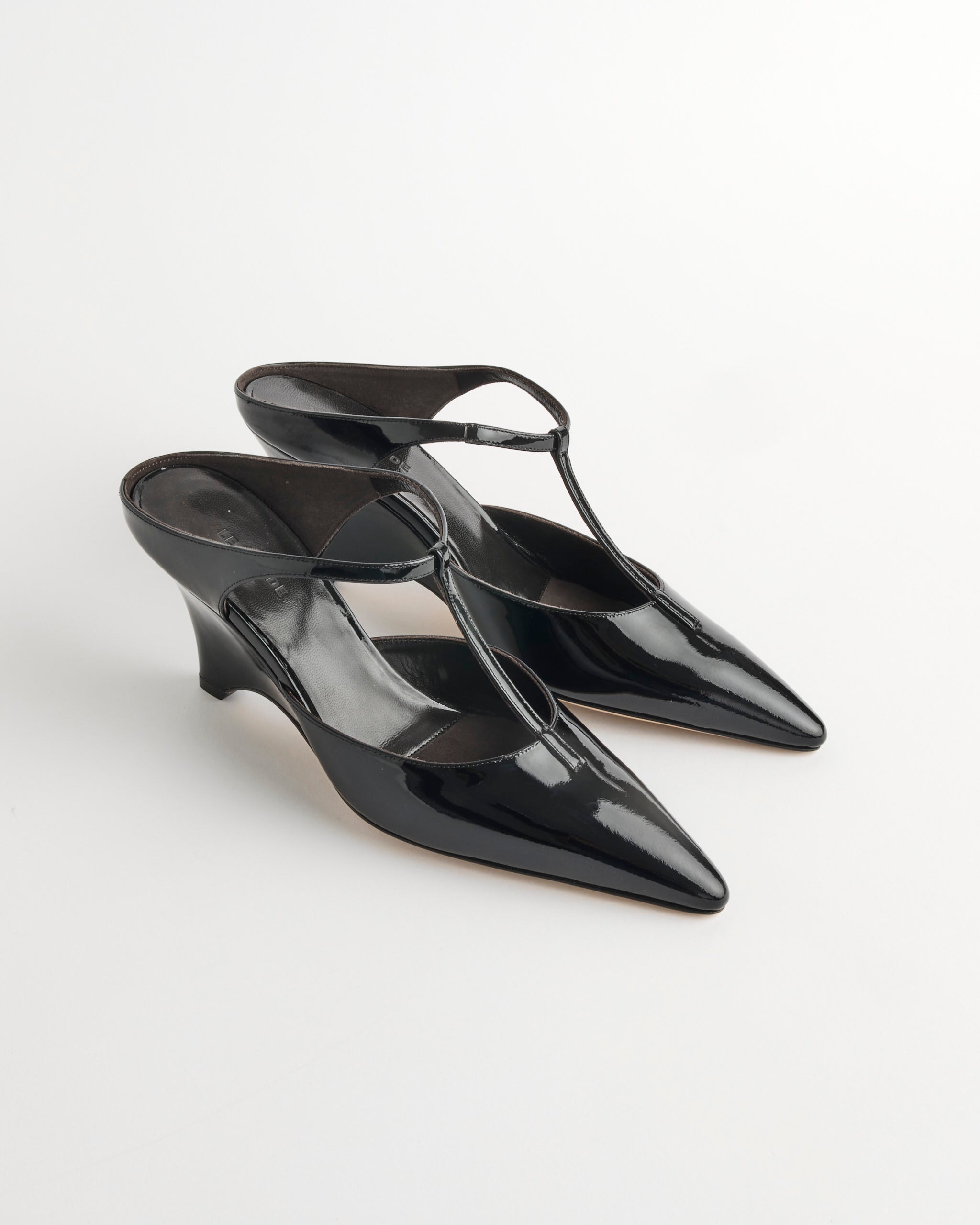 The Le Monde Beryl Victoria T-Bar Wedge in Black features shiny vernice leather, pointed toes, a low wedge heel, and thin straps, beautifully displayed on a plain white background.