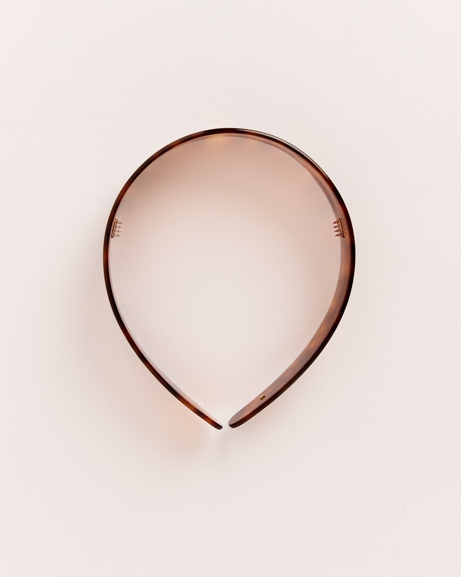 The Thin Bessette Headband in Tortoise by Sophie Buhai, made of brown tortoiseshell plastic, rests on a plain light background in an open circular shape.