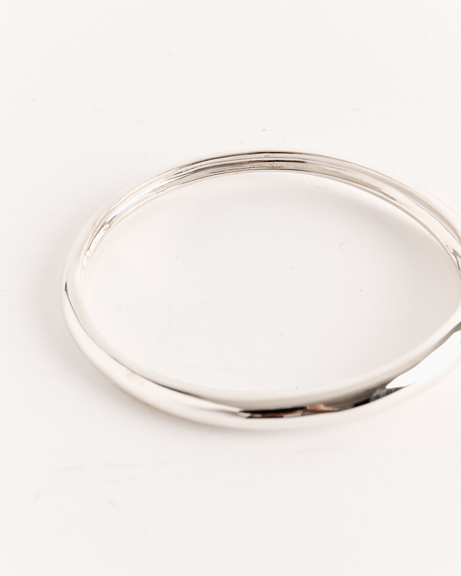 The Delicate Amorphous Bangle in Sterling Silver by Sophie Buhai rests on a white surface, beautifully highlighting the timeless elegance of Los Angeles-inspired jewelry.