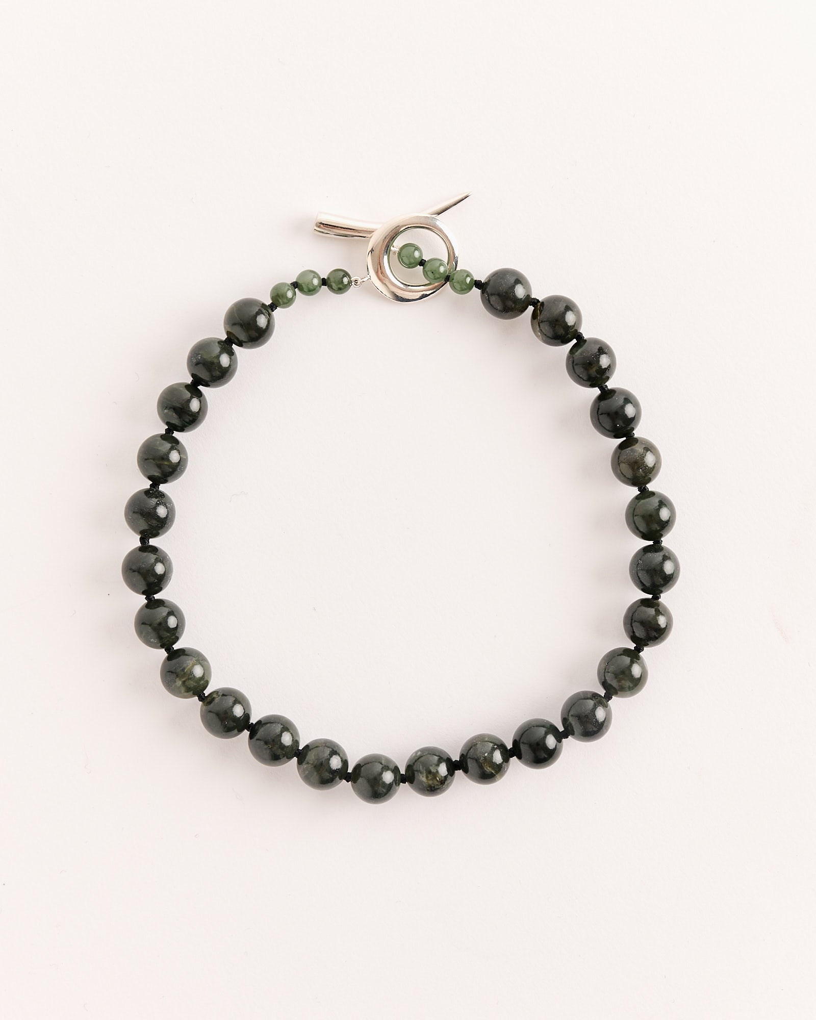 The Sophie Buhai Everyday Boule Collar in Jade features polished dark green stones and a silver toggle clasp, displayed in a circular arrangement on a plain light background. For sizing help, use our online chat to find your perfect fit.