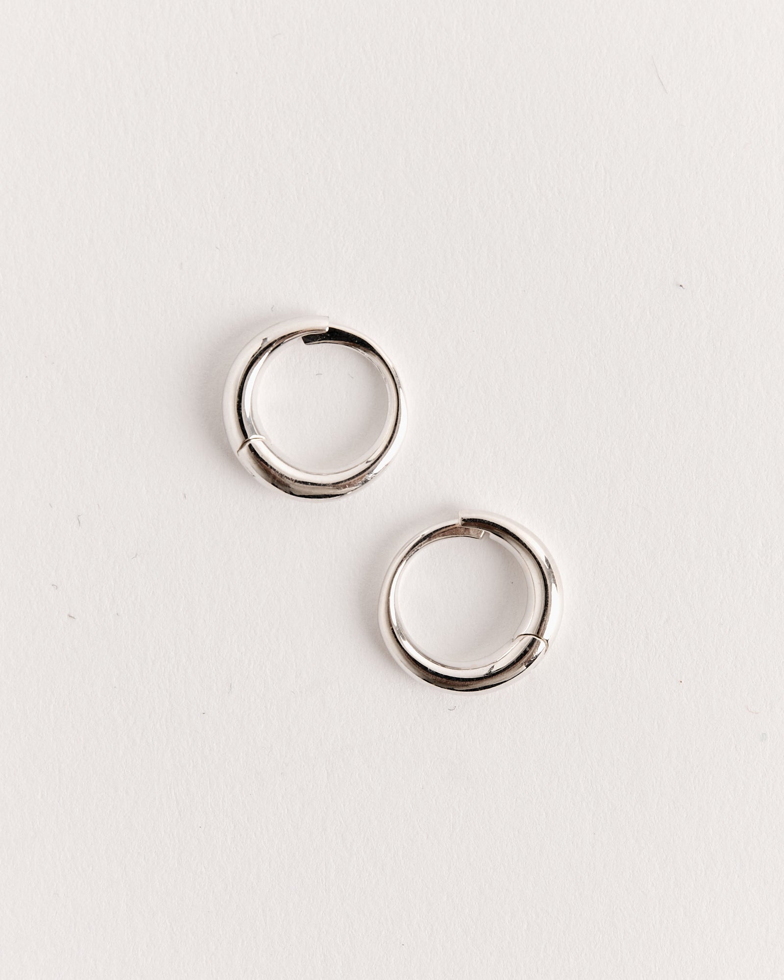 The Sophie Buhai Medium Nouveau Hoops in Sterling Silver are displayed on a plain white surface, arranged diagonally—sleek and lightweight hoop earrings ideal for everyday wear.