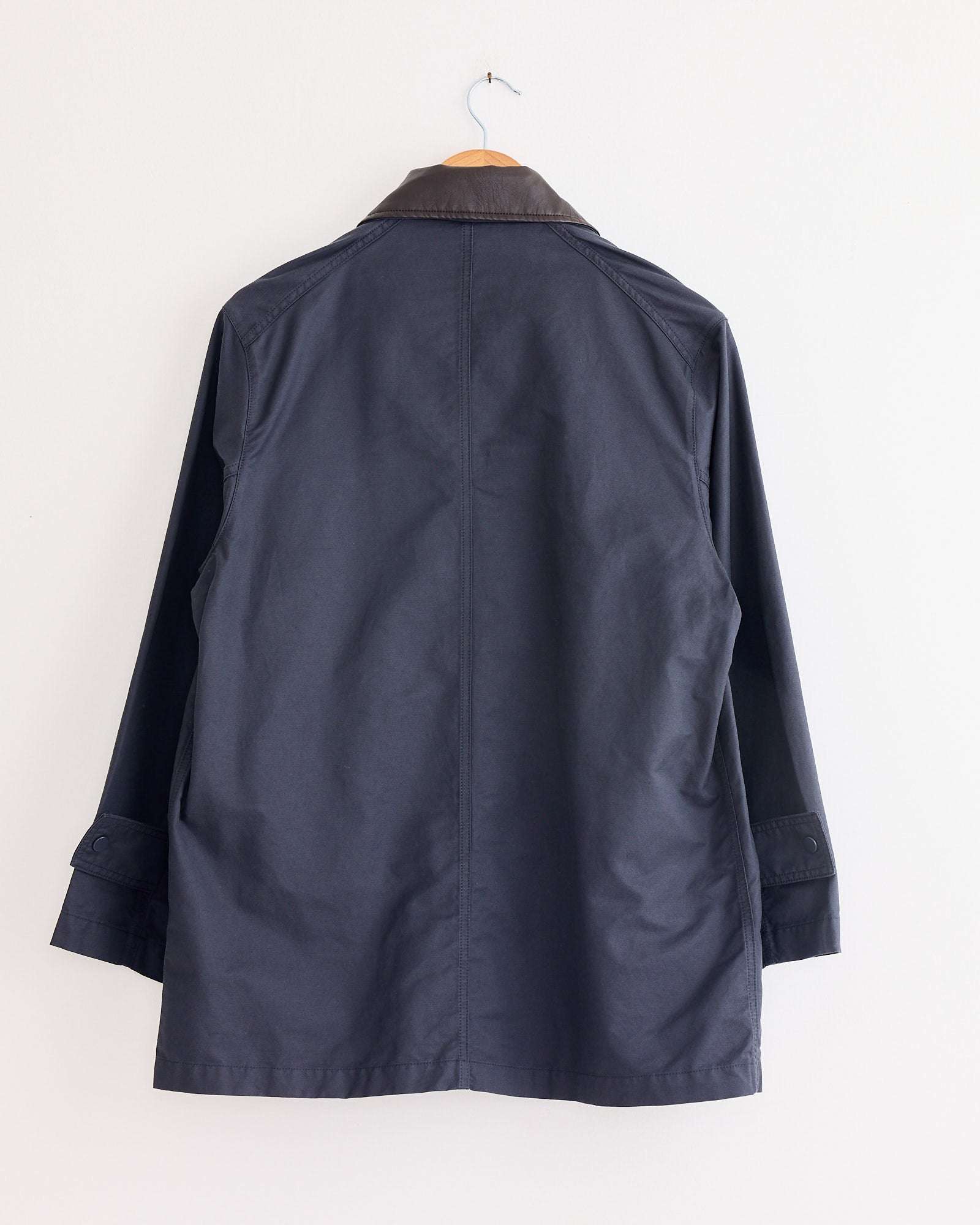 The Mijeong Park Contrast Collar Work Jacket in Navy hangs on a wooden hanger against a plain white wall, displayed from the back.