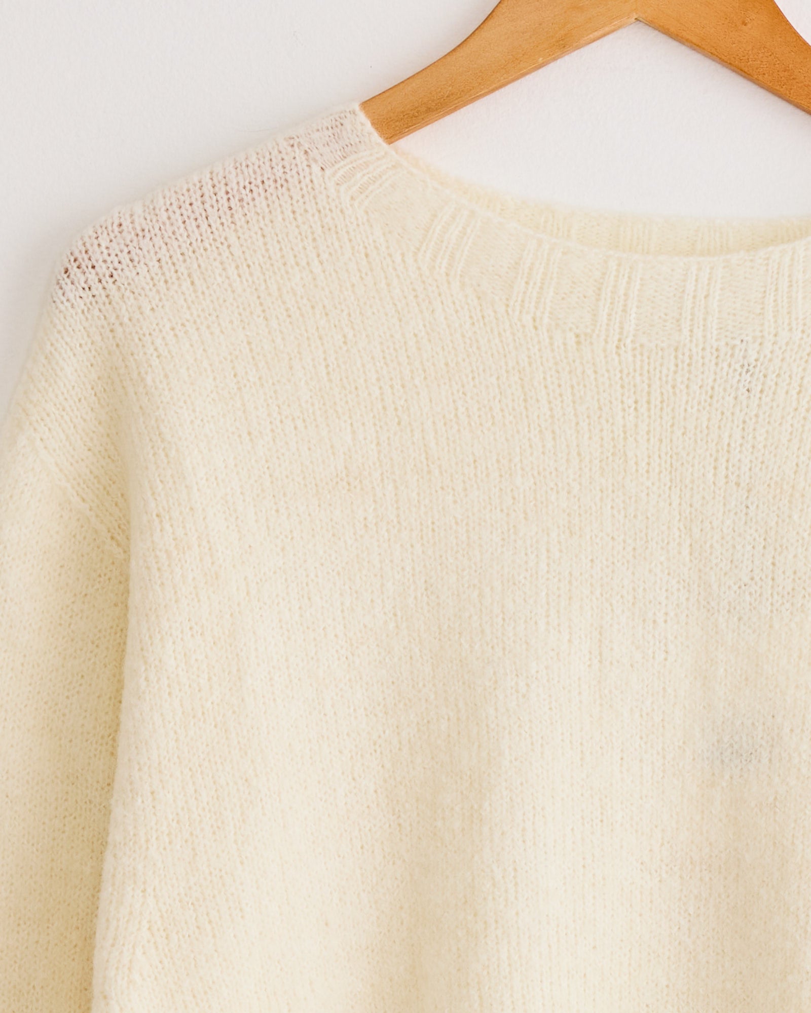 A close-up of the Mijeong Park Alpaca Blend Wholegarment Knit in Ivory on a wooden hanger, highlighting its soft texture, ribbed neckline, and luxurious alpaca blend.