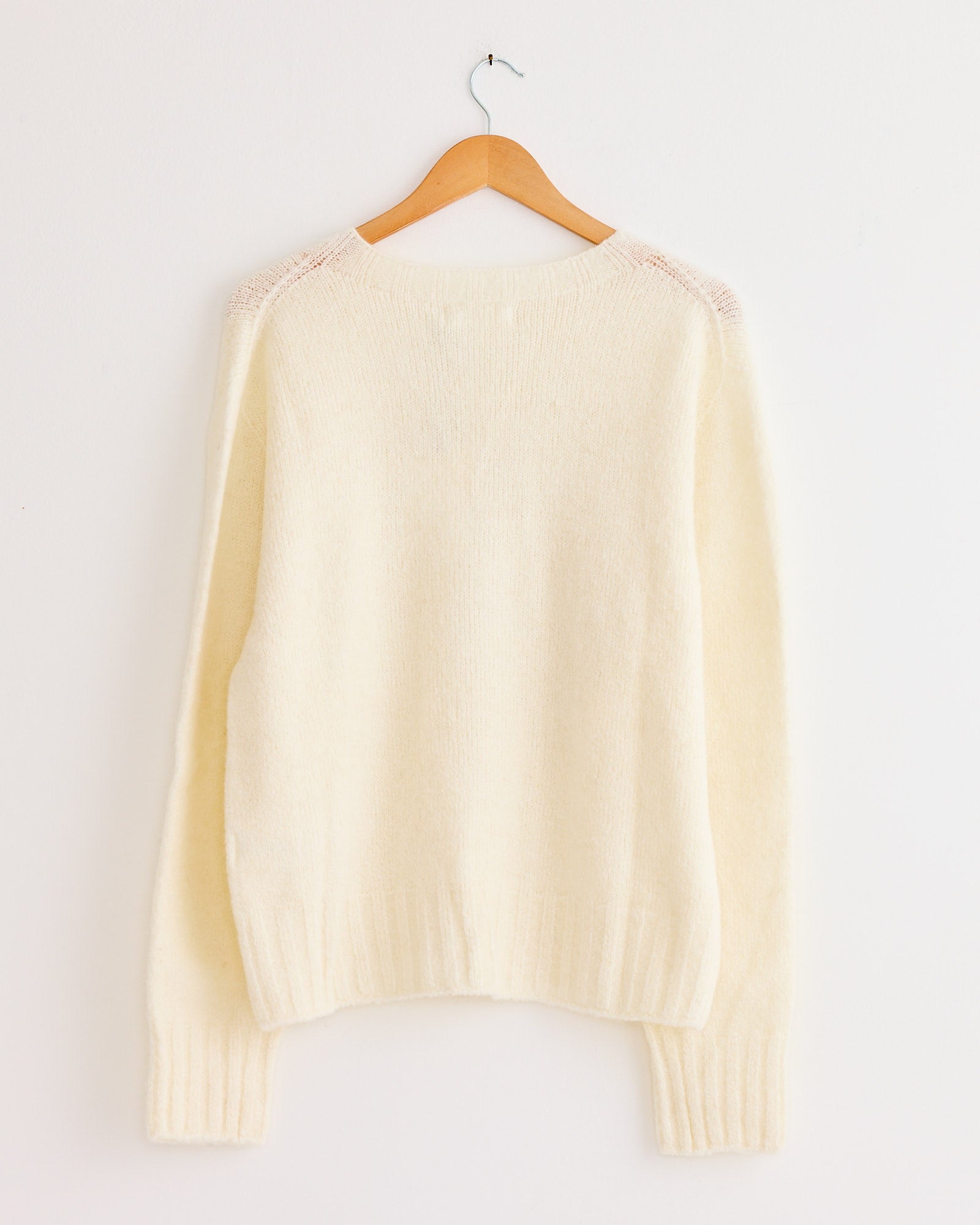 The Mijeong Park Alpaca Blend Wholegarment Knit in Ivory, an oversized sweater with long sleeves, is displayed on a wooden hanger against a plain white wall.