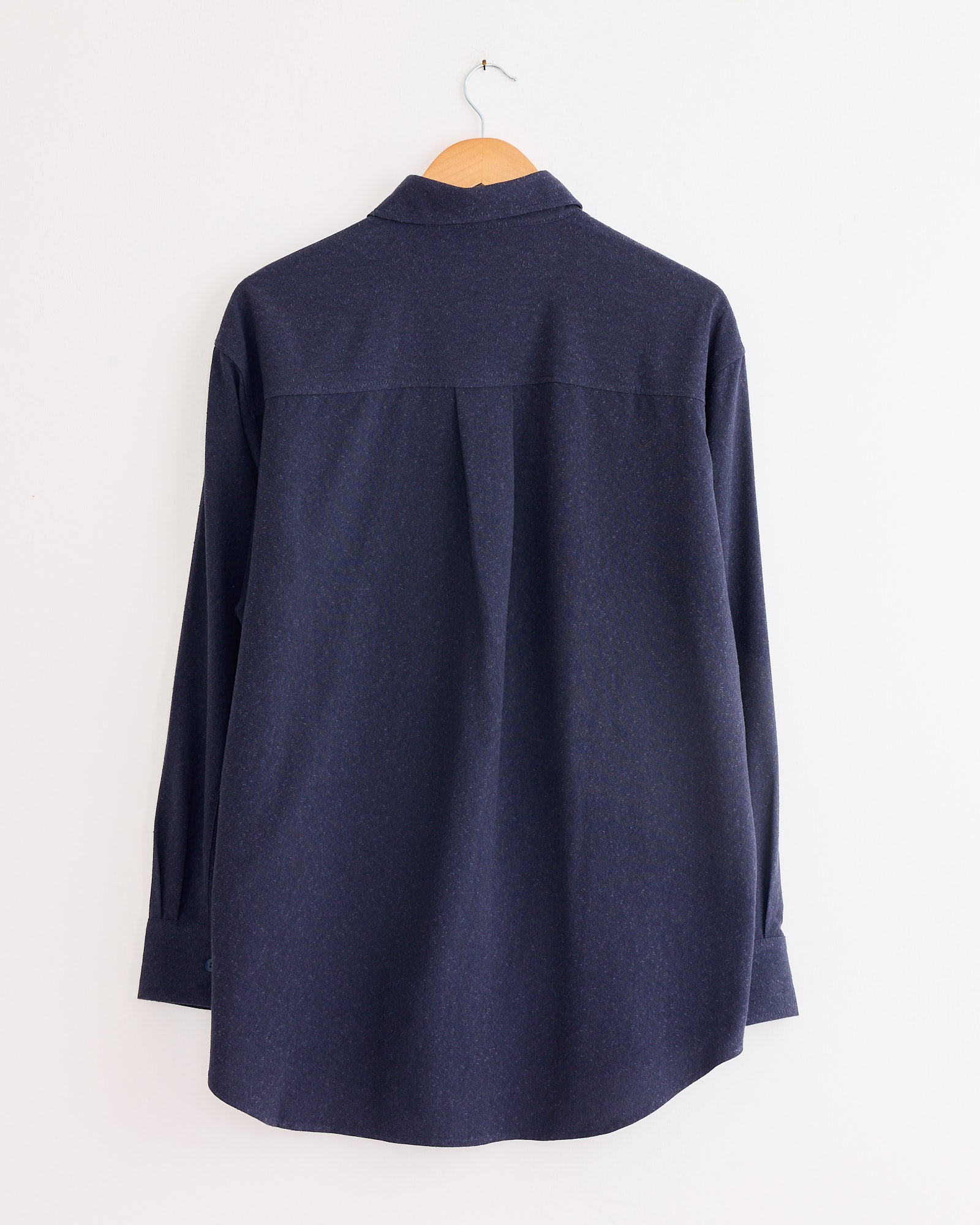 The Mijeong Park Textured Oversized Shirt in Navy, shown from the back on a wooden hanger against a white wall, features long sleeves and a cotton blend—ideal as a layering piece for effortless style.