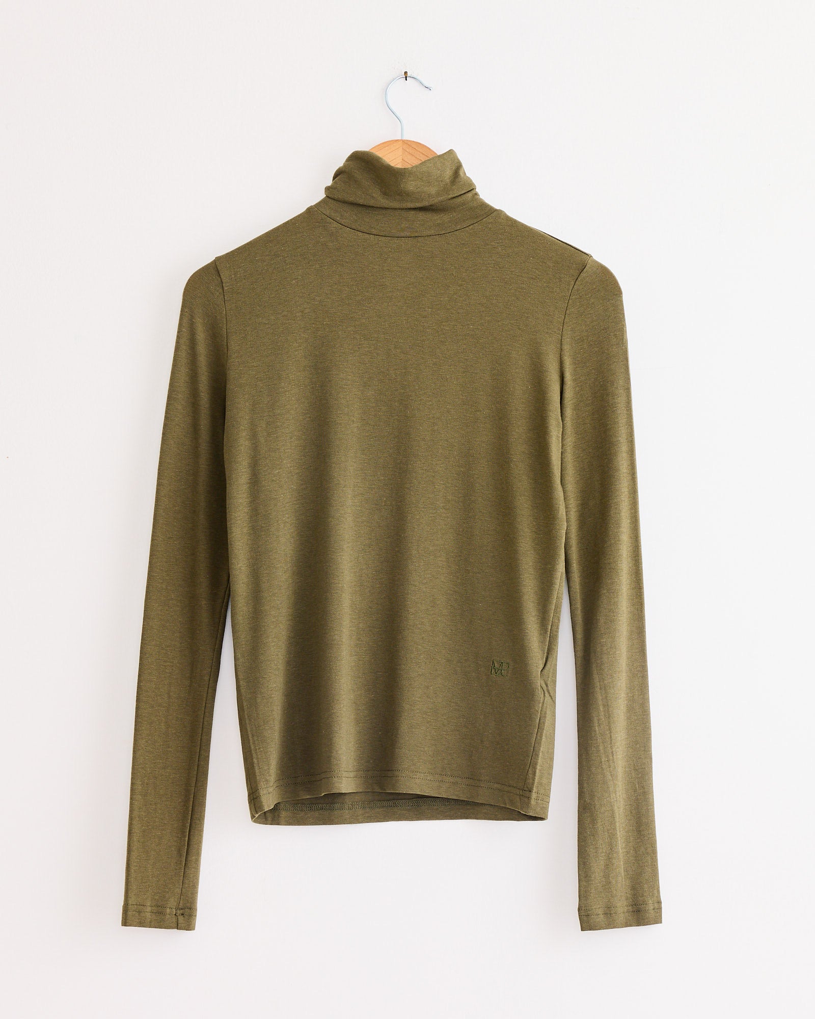 The Roll Neck Jersey Top Light in Olive by Mijeong Park features a slim fit and lightweight jersey blend, displayed on a wooden hanger against a plain white wall.