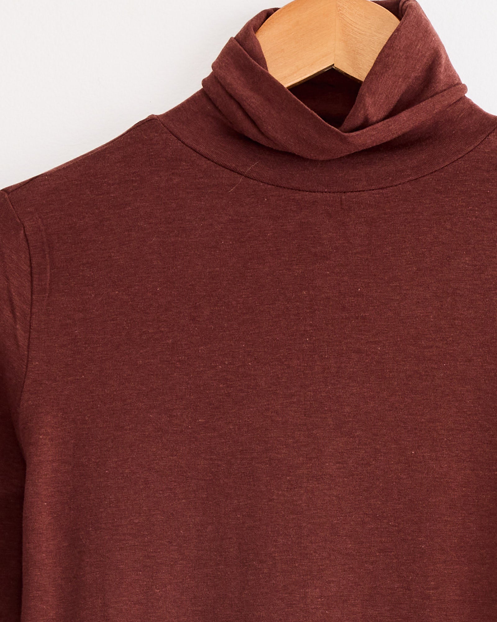 A close-up of the Mijeong Park Roll Neck Jersey Top in Burgundy, featuring a slim fit and lightweight jersey blend, displayed on a wooden hanger against a plain white background.