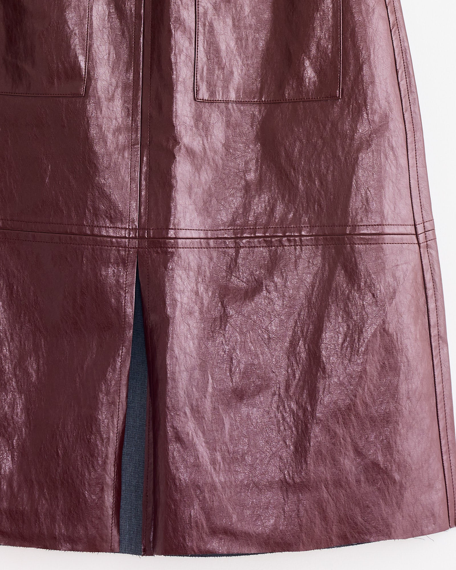 The Mijeong Park Faux Leather Skirt in Burgundy features a shiny, crinkled texture, two front pockets, a center slit, and a knee-length A-line silhouette.