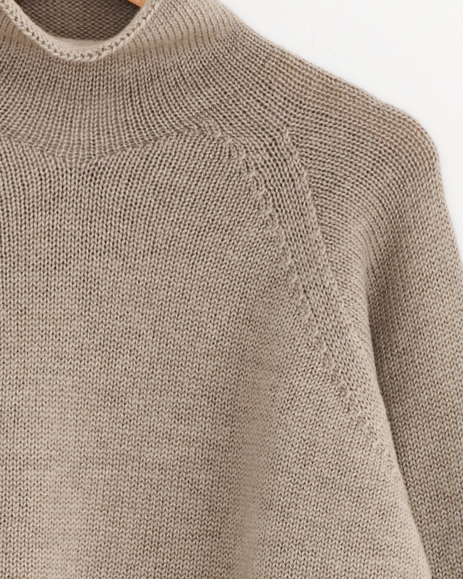 Close-up of the Rolled Edge Roll Neck in Taupe by MHL by Margaret Howell, an oversized wool sweater with a high neckline, visible stitching, and smooth Japanese spun wool. Image highlights the upper chest and shoulder.