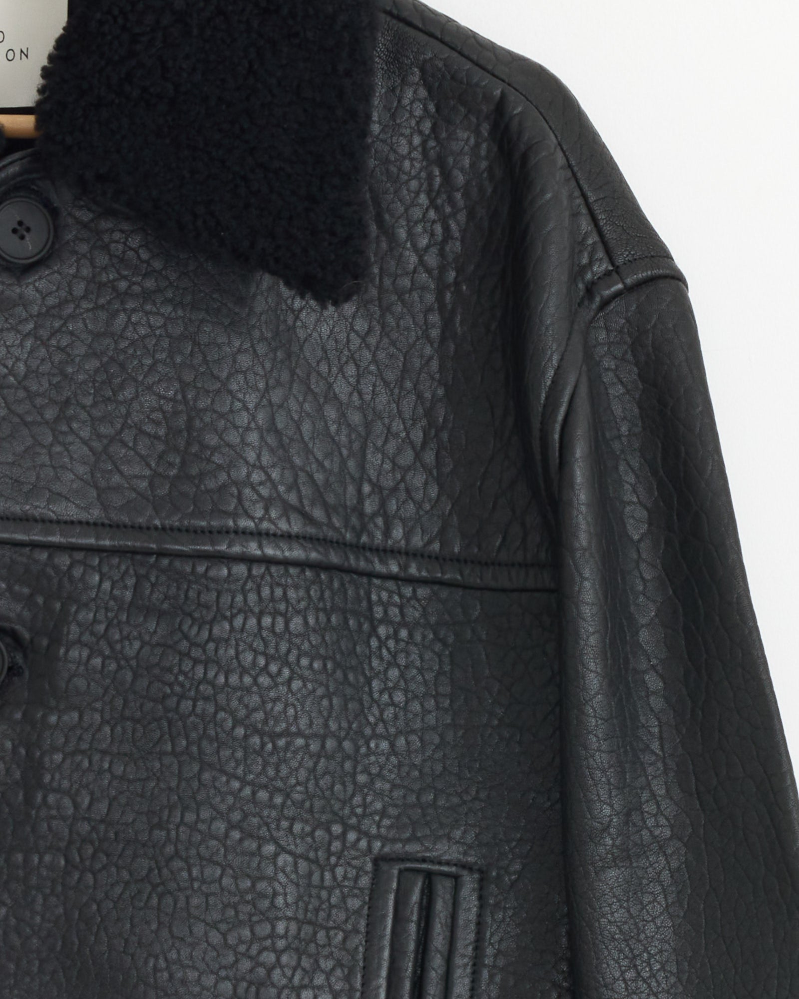 Close-up of the Del Jacket in Black by Studio Nicholson, featuring soft sheepskin leather, a detachable shearling collar, chest seam, and vertical slit pockets. Only the upper half and left side are shown.