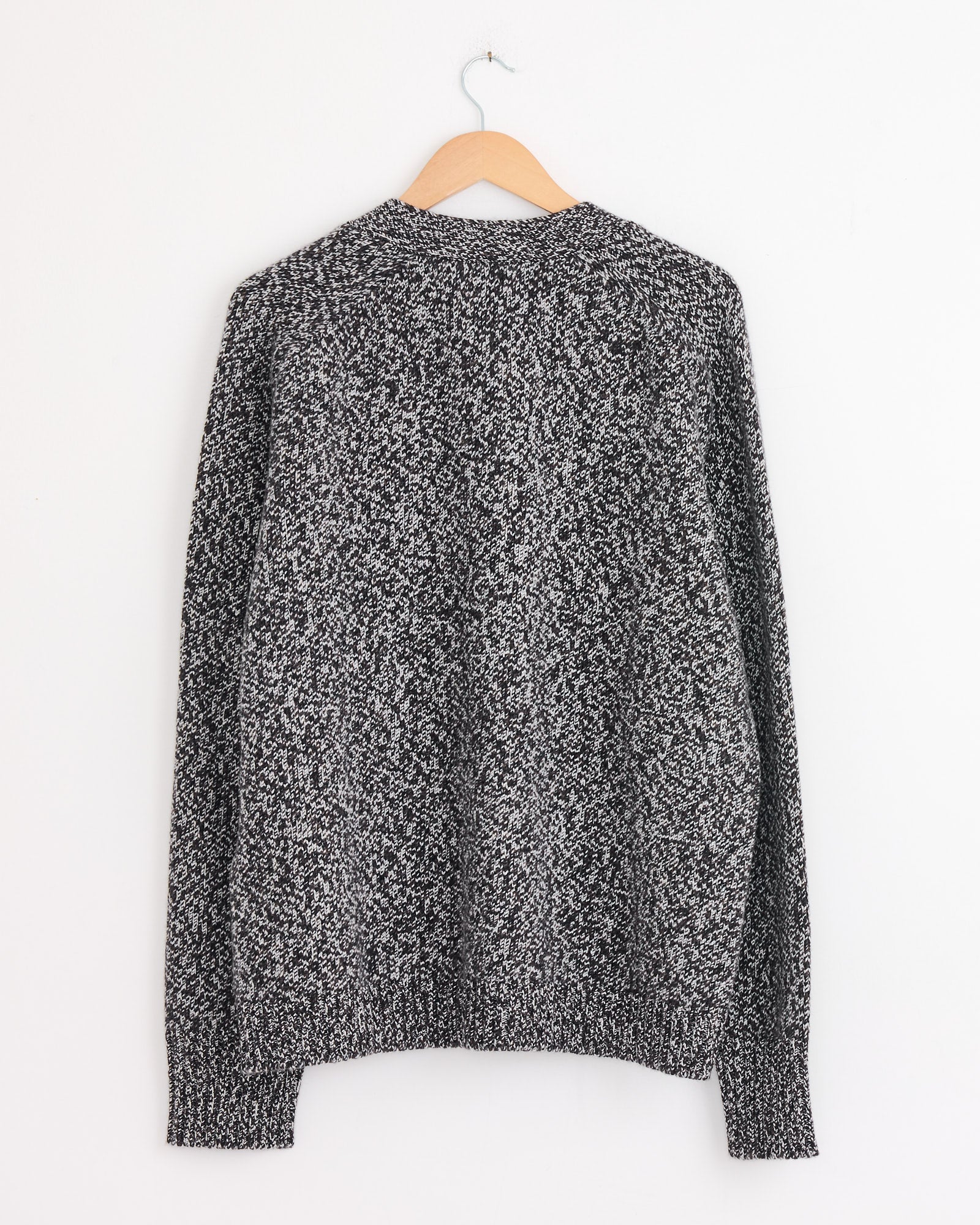 The Sen Cardigan in Navy Mouline by Studio Nicholson, a heavyweight knit, hangs on a wooden hanger against a plain white wall and is shown from the back.