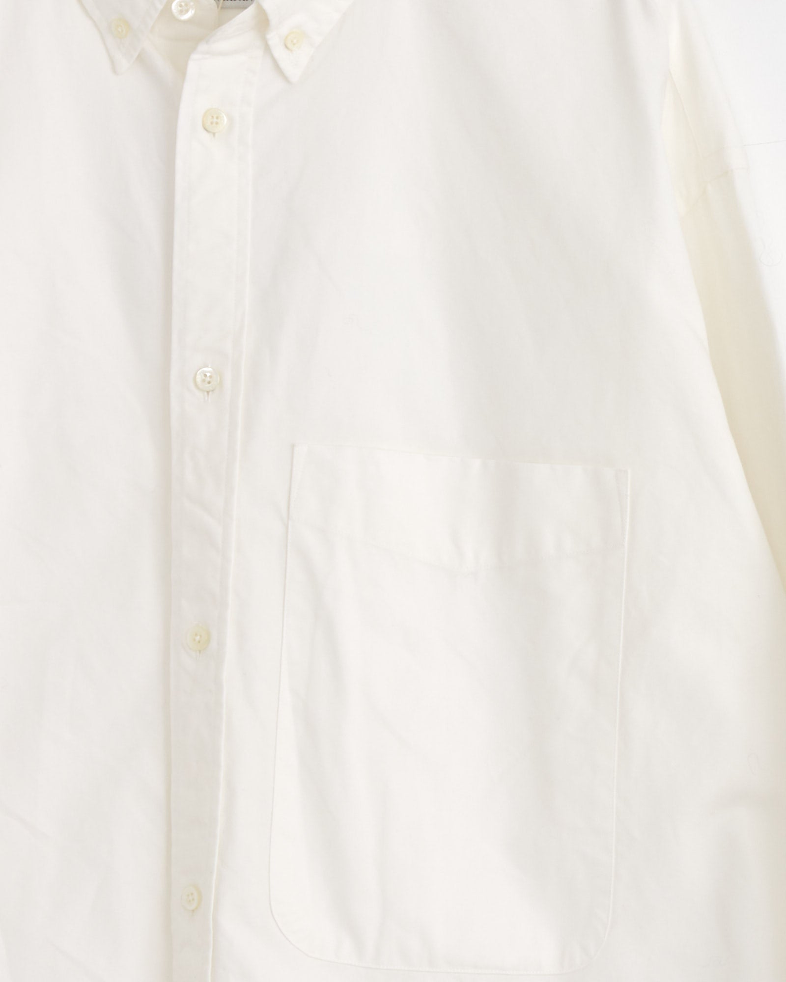 A close-up of the Studio Nicholson x BEAMS PLUS Lisa Shirt in White, an Oxford shirt made in Japan with a left front pocket and cream buttons.