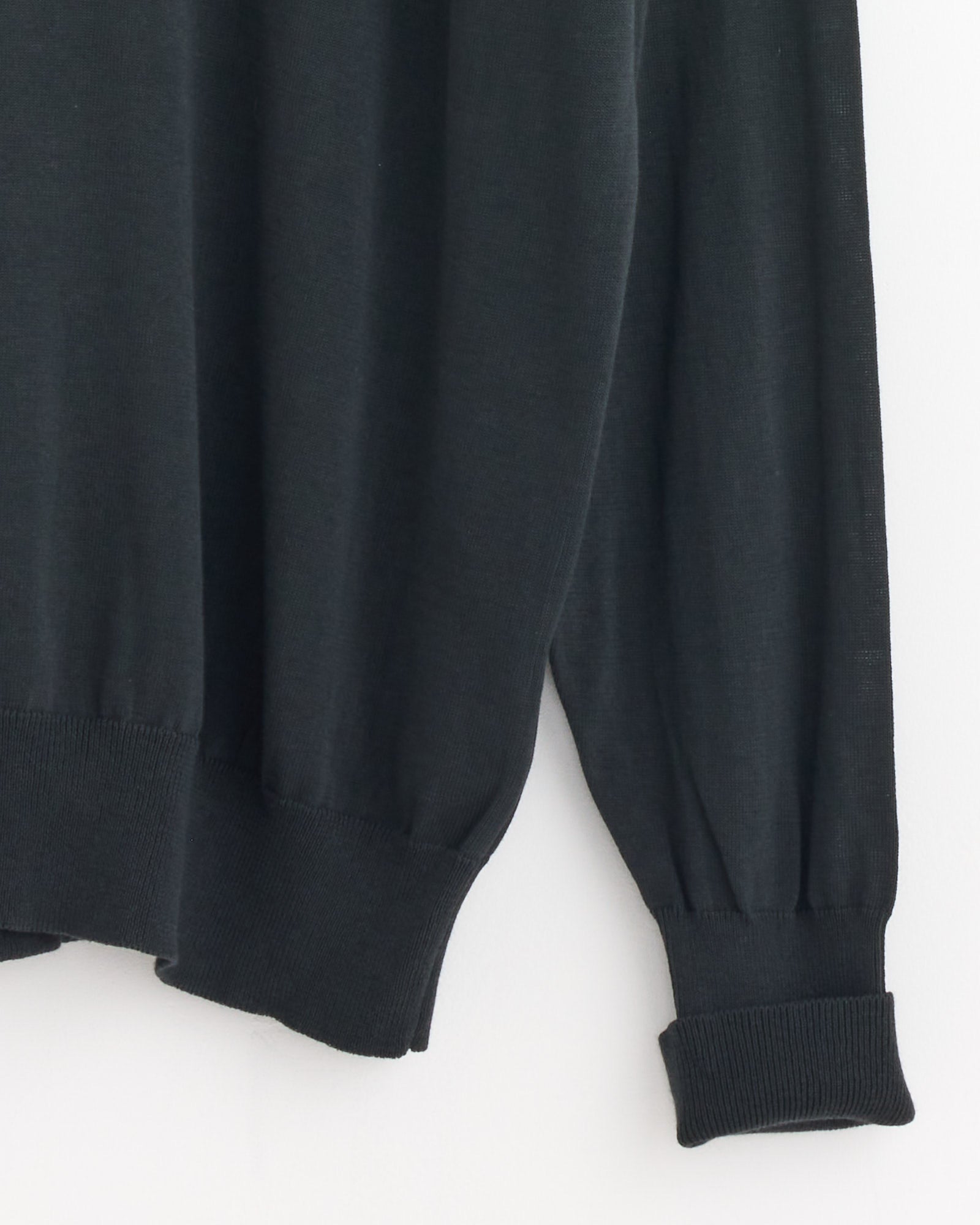 A close-up of the lower part of the Still By Hand Cotton Silk Pullover in Green Charcoal, highlighting its ribbed cuffs and hem against a plain white background.