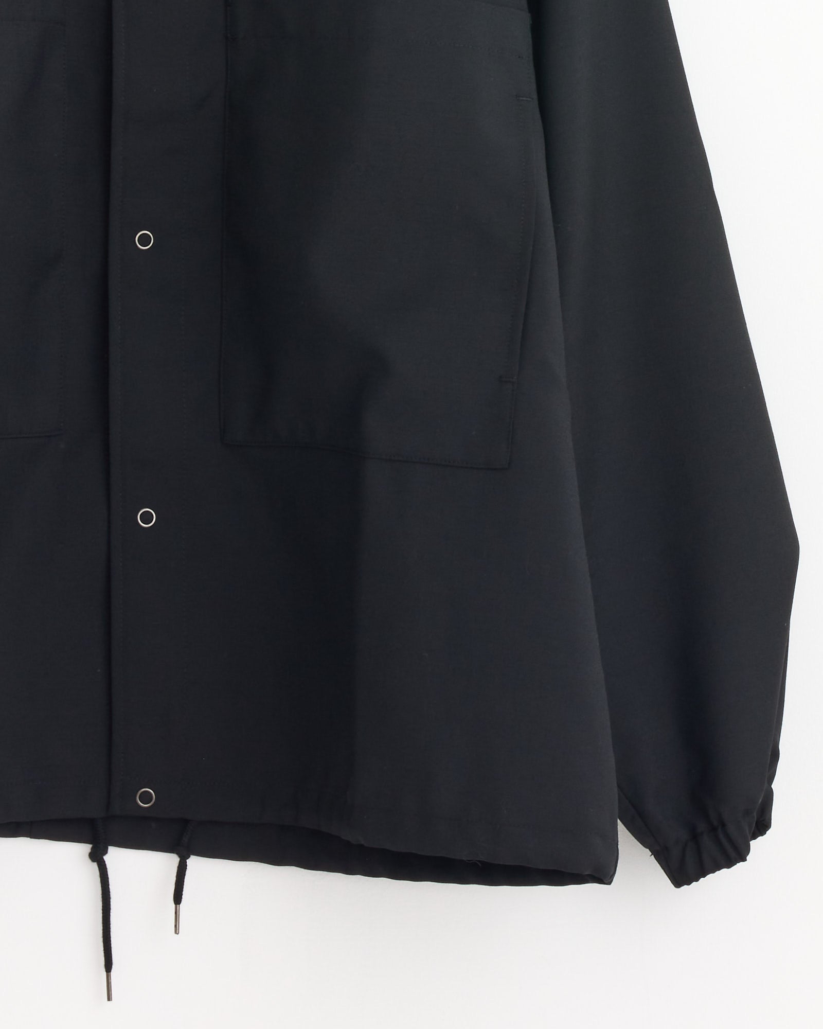 A close-up of the Double Pocket Shirt Jacket in Ink Black by Still By Hand, featuring snap buttons, large front pockets, elastic cuffs, and a drawstring hem. Made in Japan, wind and water resistant, shown on a plain white background.