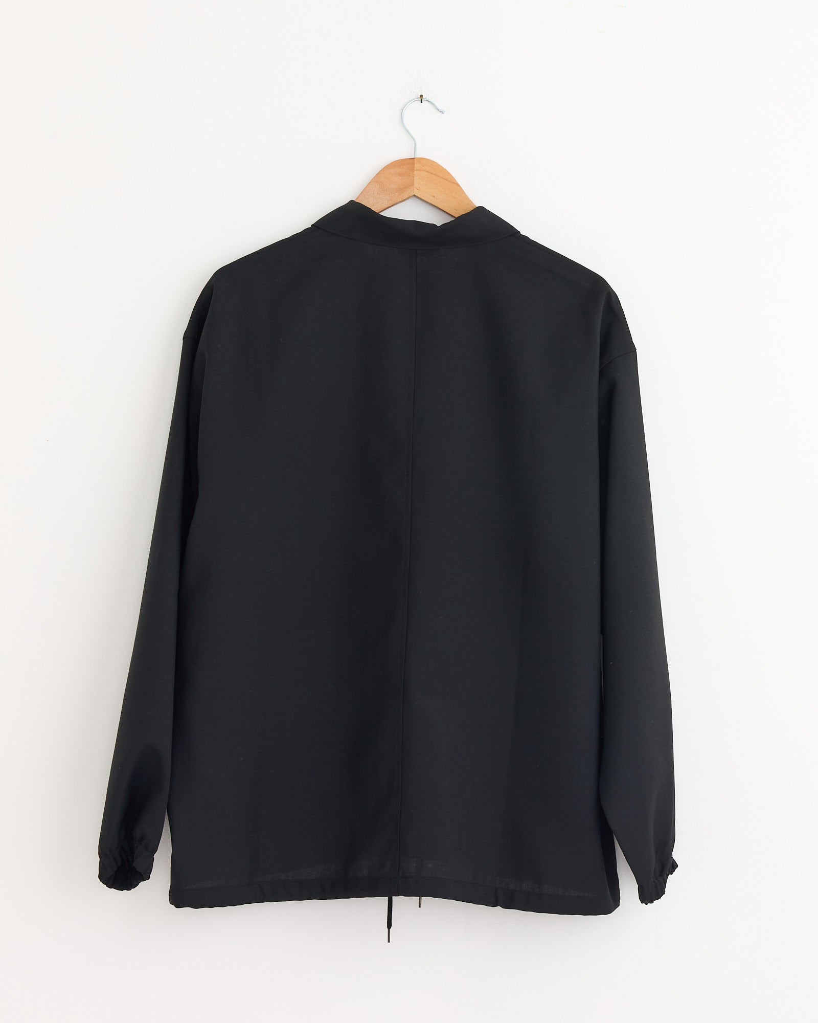 The Still By Hand Double Pocket Shirt Jacket in Ink Black, made in Japan, is displayed from the back on a wooden hanger against a plain white wall.
