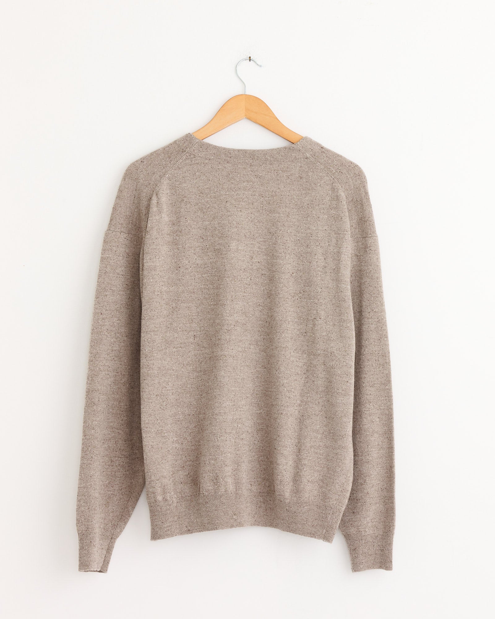 The Still By Hand Silk Mixed 2B Cardigan in Sand Beige, long-sleeved, hangs from a wooden hanger against a plain white wall, seen from the back.