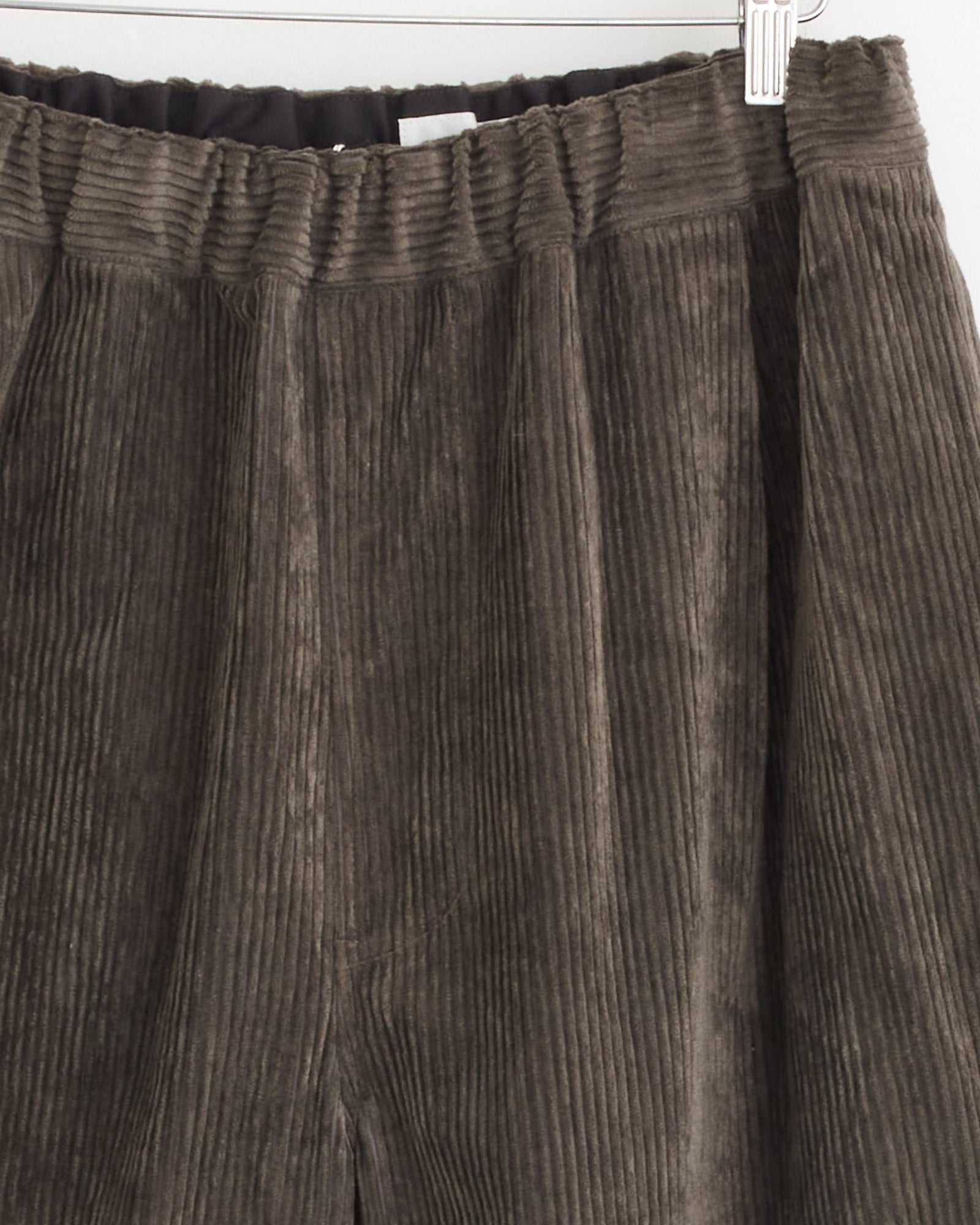 Close-up of Still By Hand’s Corduroy Easy Pant in Khaki Brown, made in Japan, featuring visible vertical ridges and an elastic waistband, displayed on a hanger.