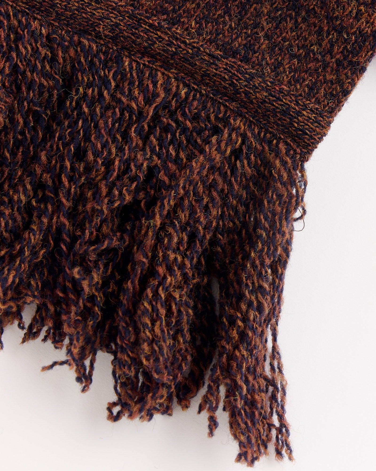 Close-up of the fringed edge on the 7G Fringe Muffler in Melange Brown by Still By Hand, highlighting twisted yarns and textured fibers in dark hues against a plain white background.