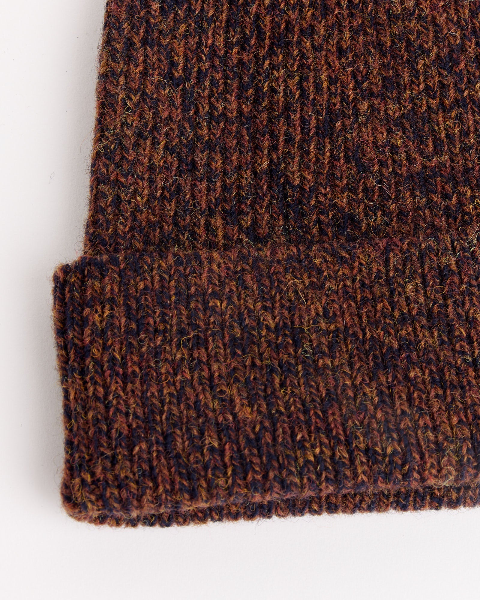 Close-up of the Still By Hand 7G Knit Cap in Melange Brown, featuring a folded brim and textured multicolored knit pattern, photographed on a white background.