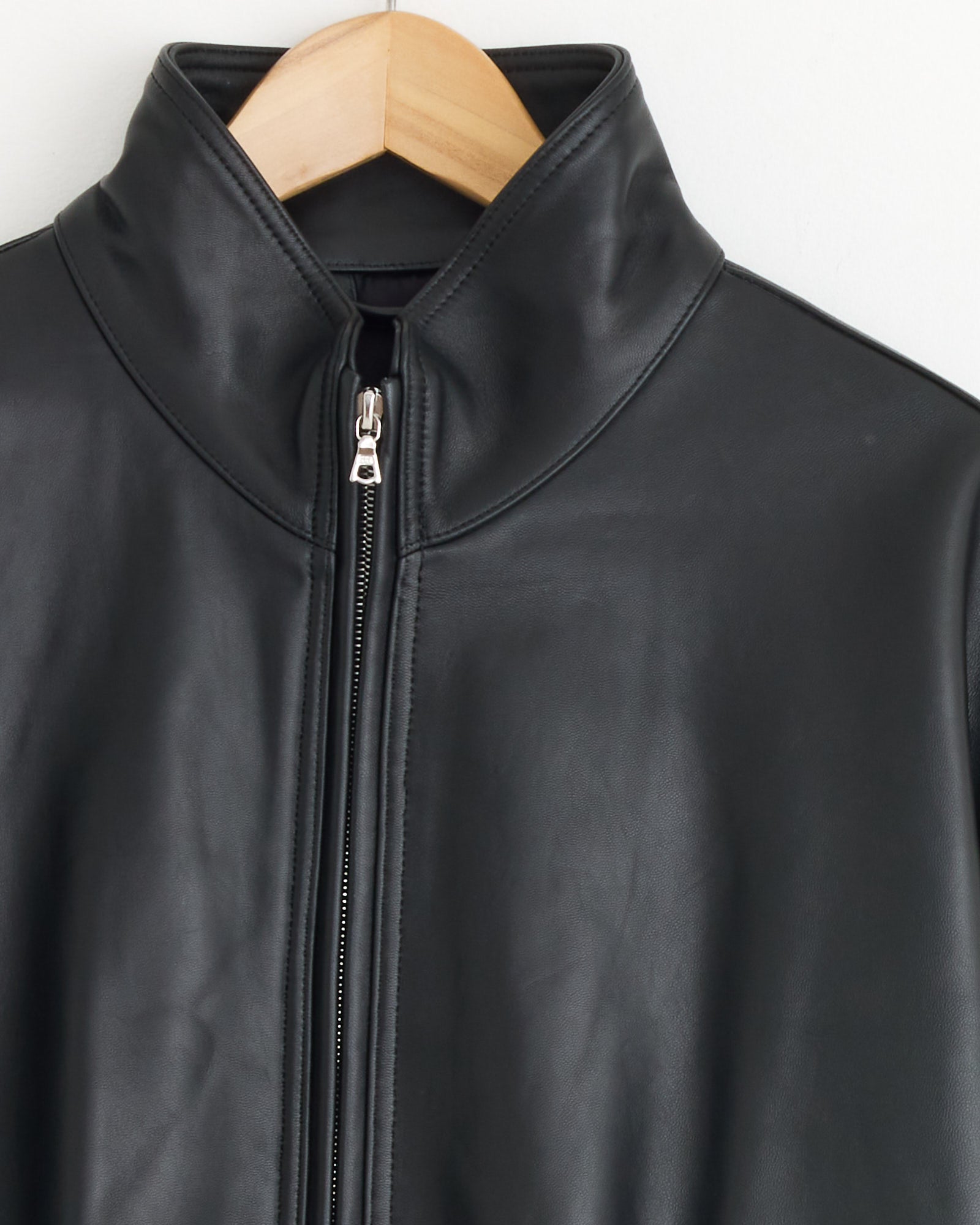 A close-up of the ssstein 1220 Leather Jacket in Black on a wooden hanger, highlighting its high collar and silver front zipper—an ideal pick for vintage jacket enthusiasts.