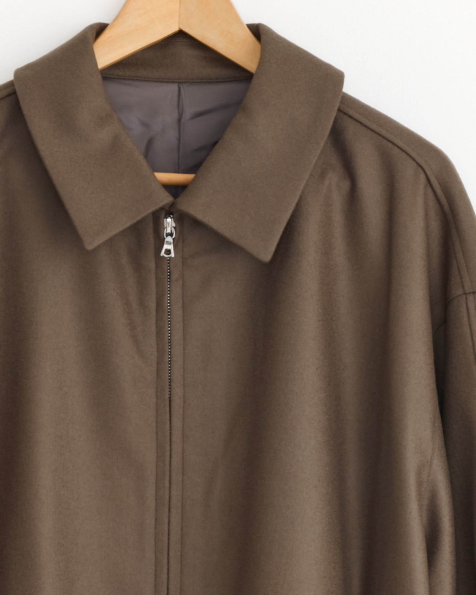 A close-up of the ssstein Melton 1226 Jacket in dark beige, featuring a wide collar and crafted from Super 120’s wool, shown hanging on a wooden hanger against a white background.