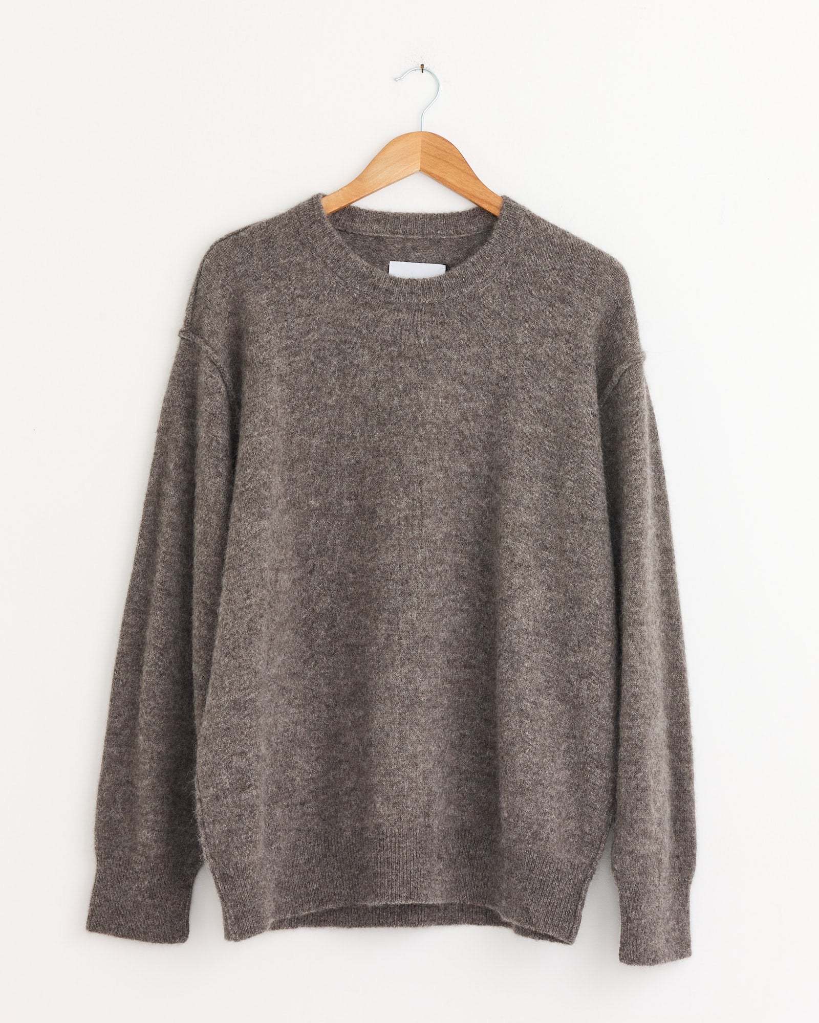 The ssstein 1294 Sweater in Greige, crafted from Geelong Lambs Wool with long sleeves, is displayed on a wooden hanger against a plain white wall.