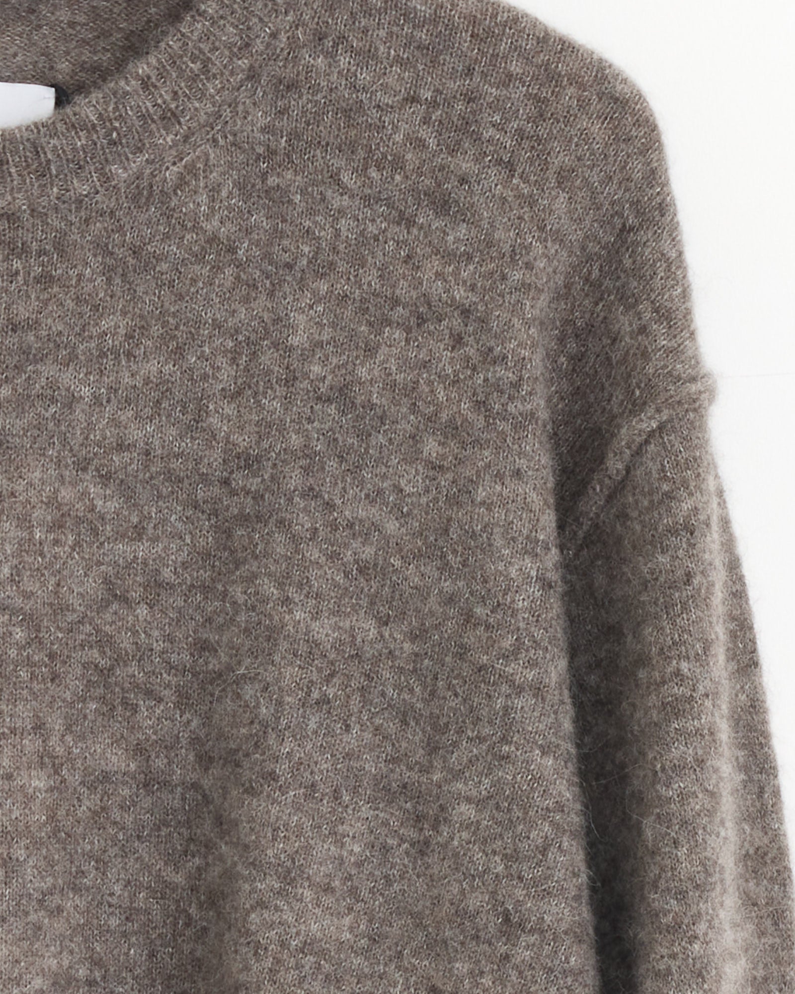 A close-up of the ssstein 1294 Sweater in Greige, a soft Baby Alpaca knit with a high neckline and long sleeves, made in Japan, hanging against a light-colored wall.